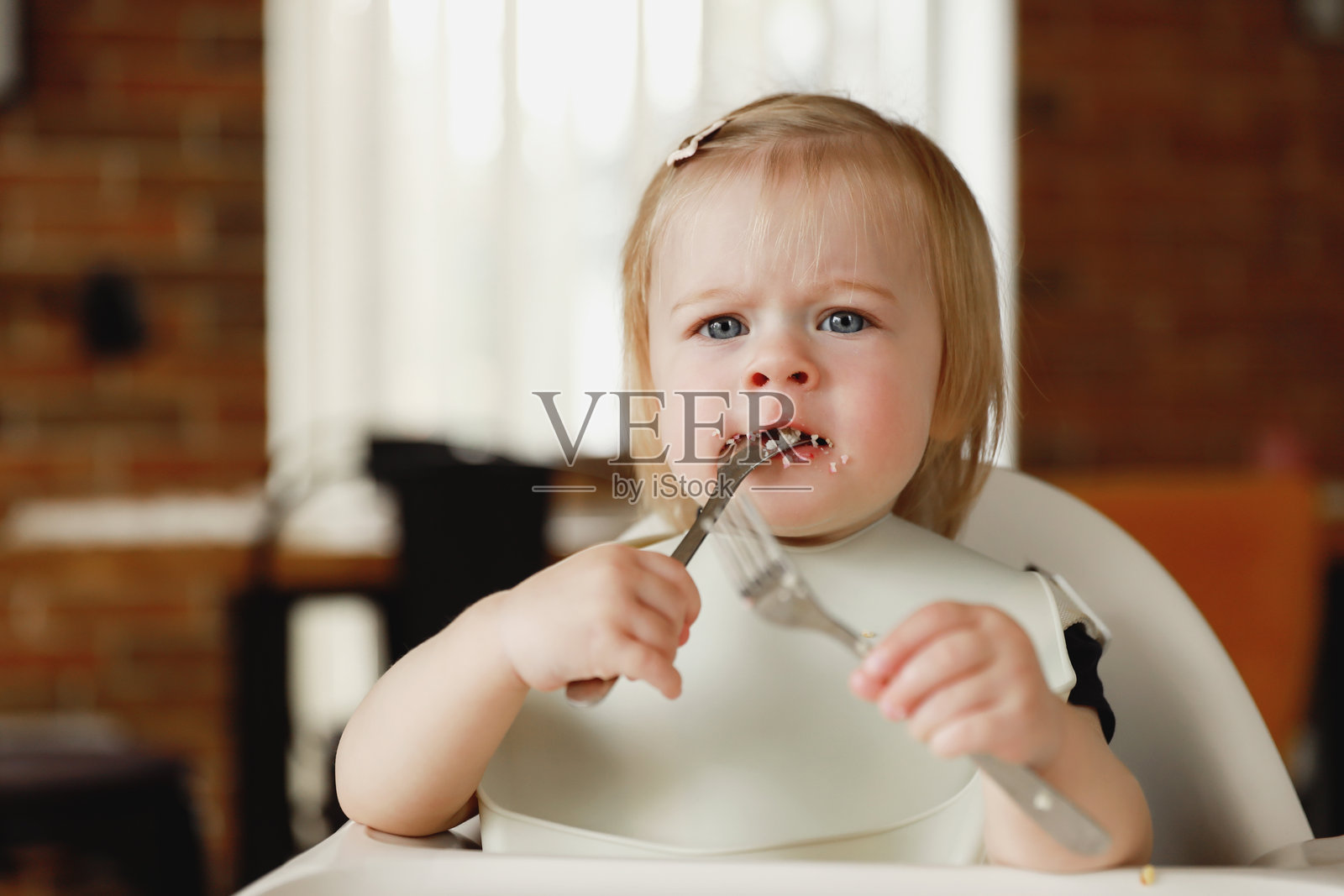婴儿女孩或幼儿坐在高脚椅上，自己用勺子吃饭。照片摄影图片