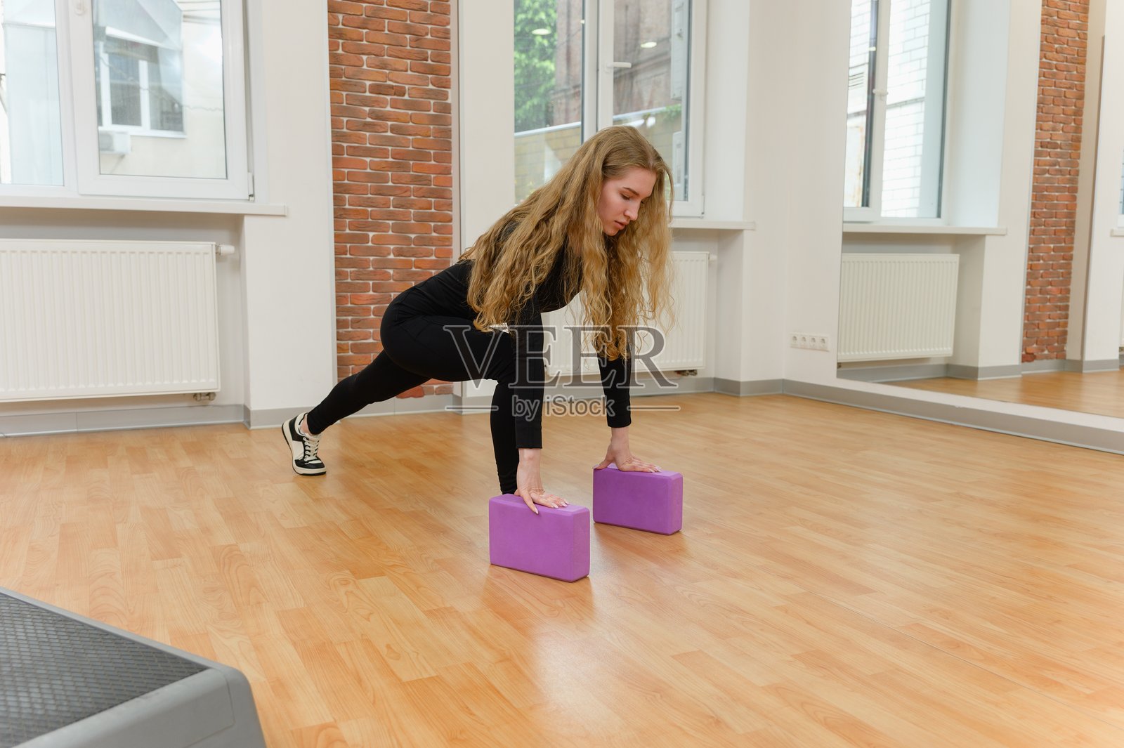 年轻女性在室内使用瑜伽砖进行拉伸。照片摄影图片
