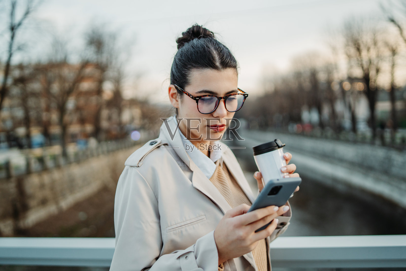 年轻的白人女性下班回家，喝着咖啡并使用手机。照片摄影图片