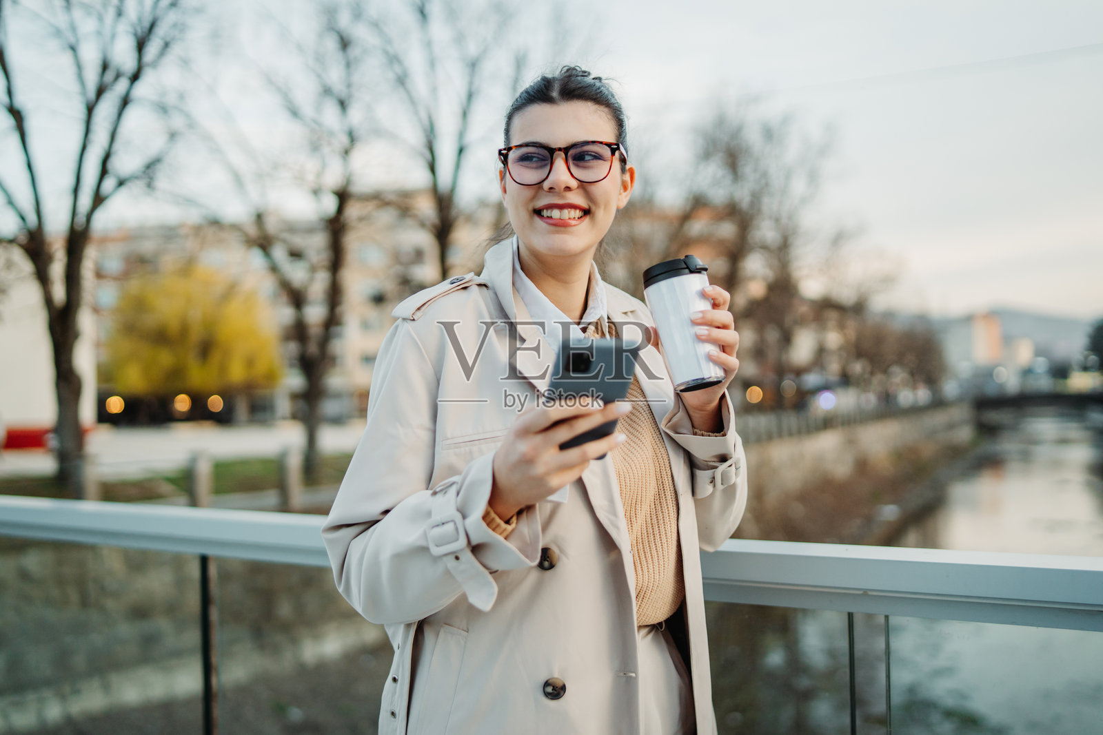 年轻的白人女性下班回家，喝着咖啡并使用手机。照片摄影图片