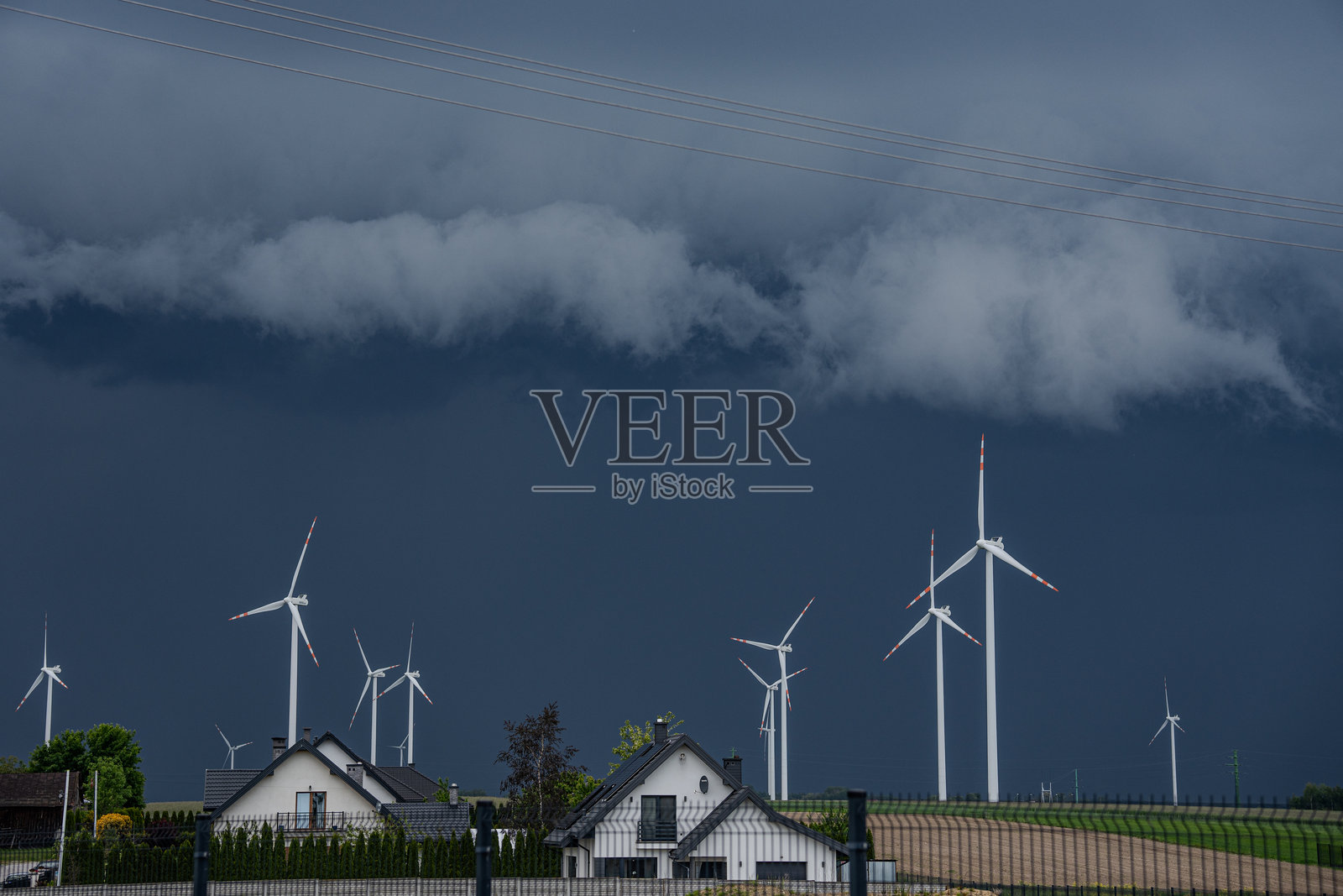 现代风力涡轮机矗立在住宅附近，背景是戏剧性的天空照片摄影图片