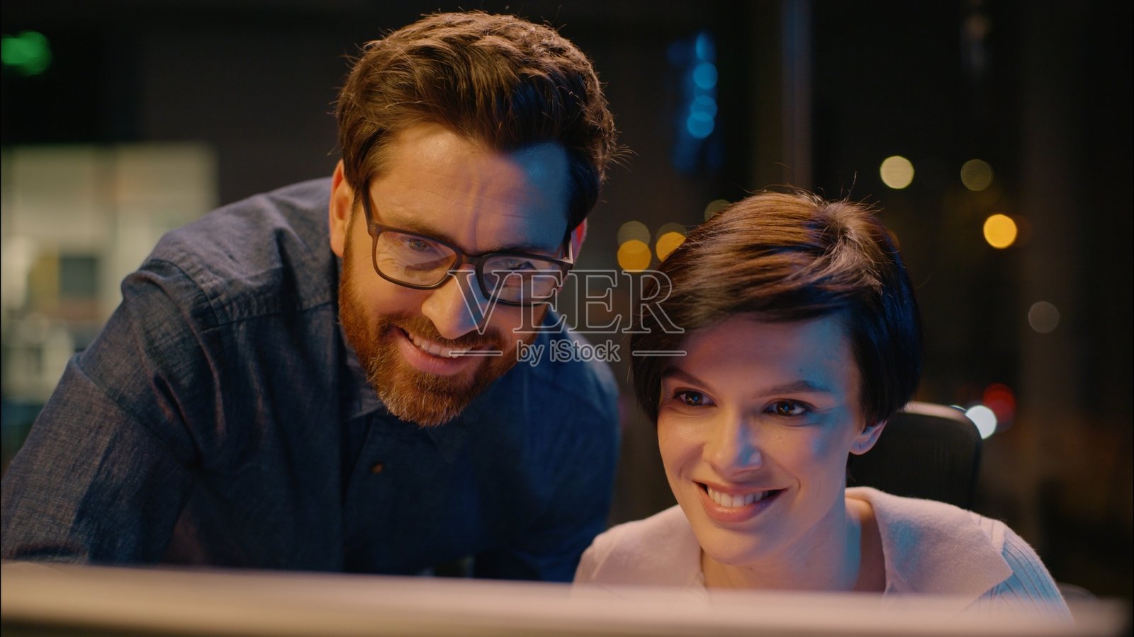 白人女商人与男商人在夜间办公室一起工作，微笑着进行高五手势，展现团队合作，成功的伙伴关系。照片摄影图片