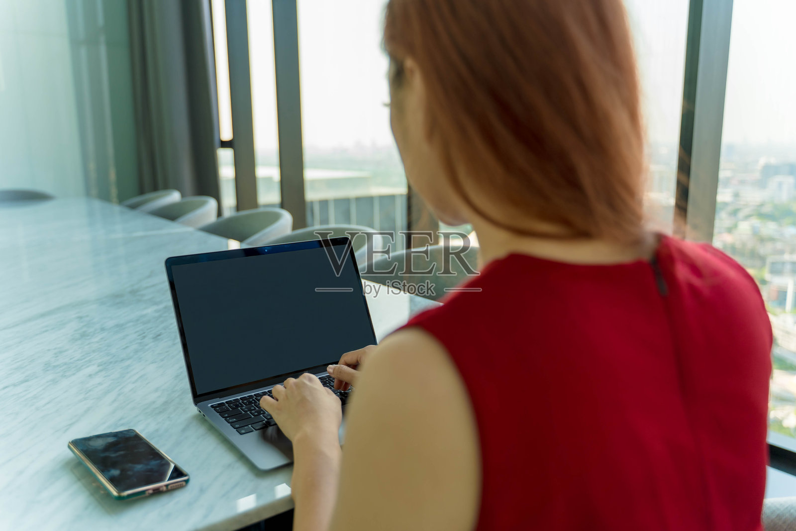 女商人在现代高层办公室中登录笔记本电脑，享受全景城市景观，专注并准备开始她高效的一天。照片摄影图片