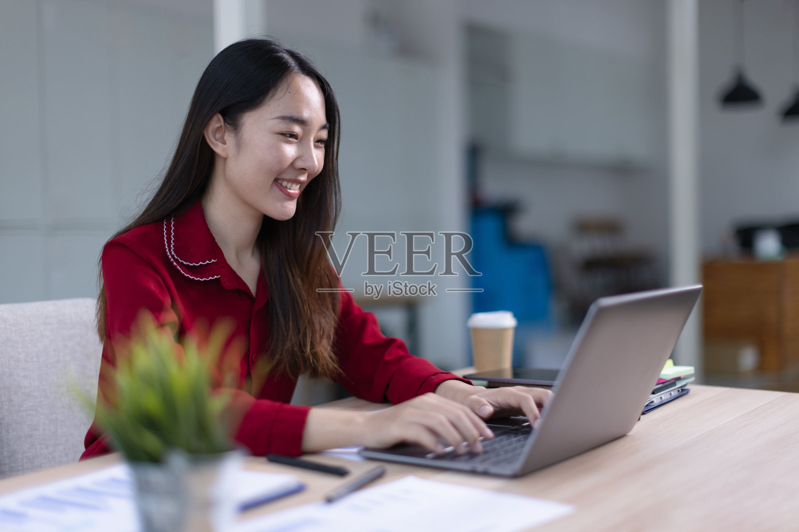 快乐兴奋的亚洲女性穿着红色衬衫在办公室工作空间。照片摄影图片