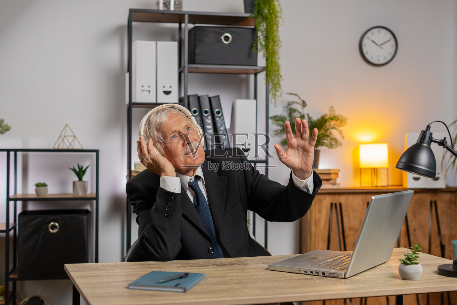 兴奋的老年商人在家办公室的桌子前戴着耳机听音乐照片摄影图片