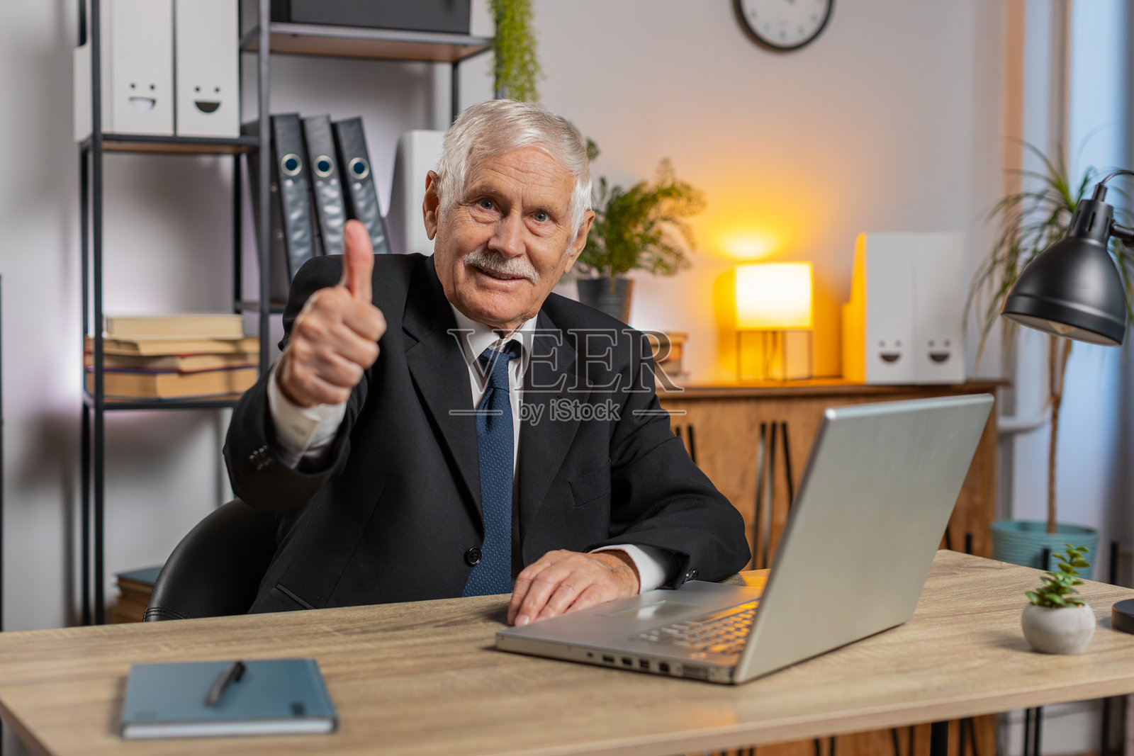 快乐的白人老年商人在家办公室使用笔记本电脑并对着镜头竖起大拇指照片摄影图片