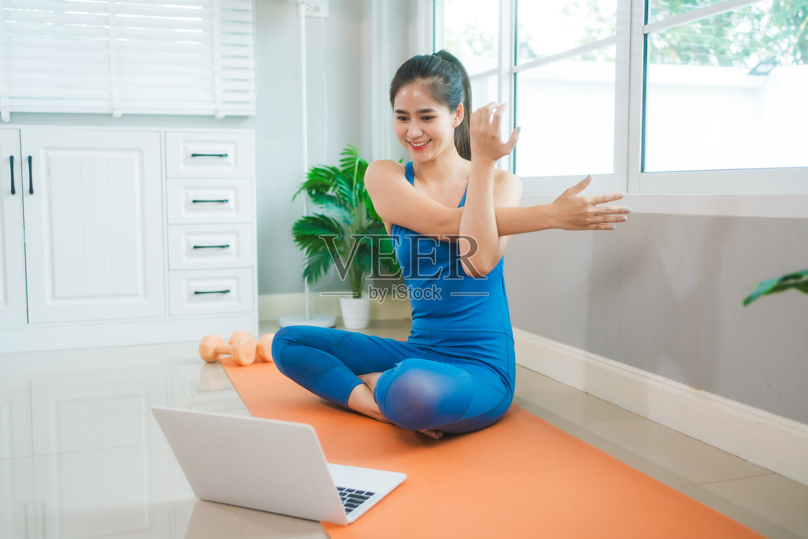 年轻的亚洲女性在家中的客厅瑜伽垫上练习瑜伽，拉伸背部。她充满挑战和动力地进行普拉提，以促进健康、健身和身心健康。照片摄影图片