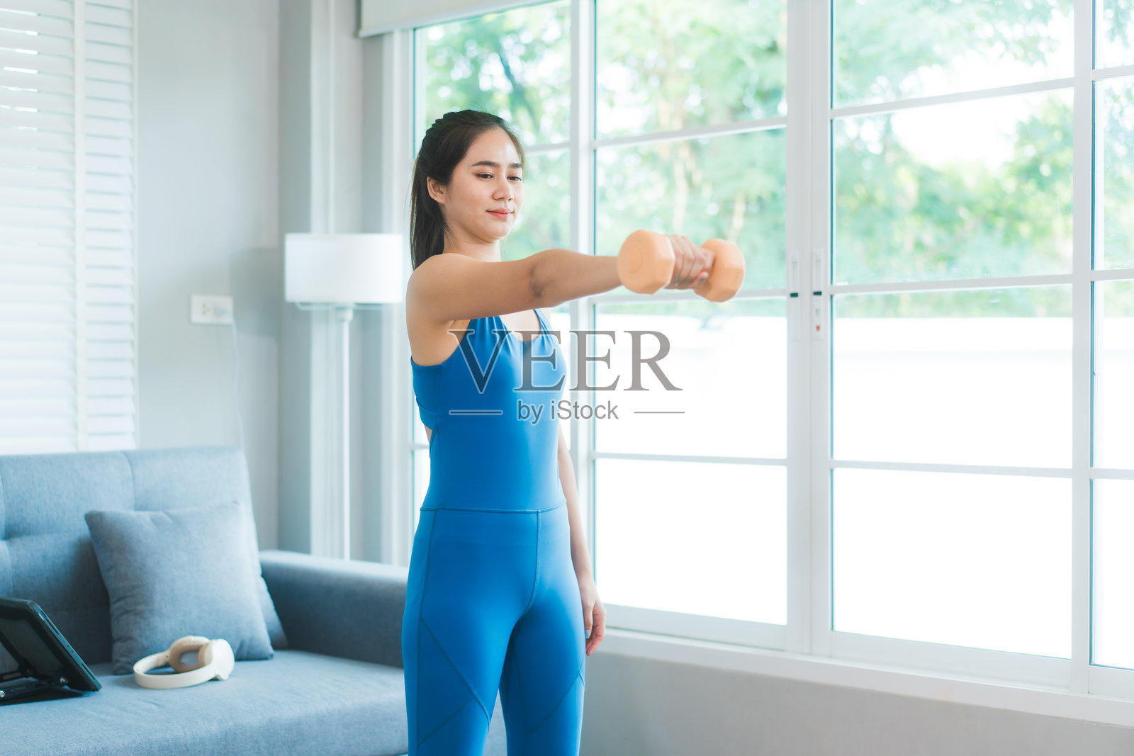 亚洲女性穿着运动服在家中使用哑铃锻炼。她的身材健美，散发着健康的气息，展现出对健身、力量训练和健康生活方式的坚持。照片摄影图片