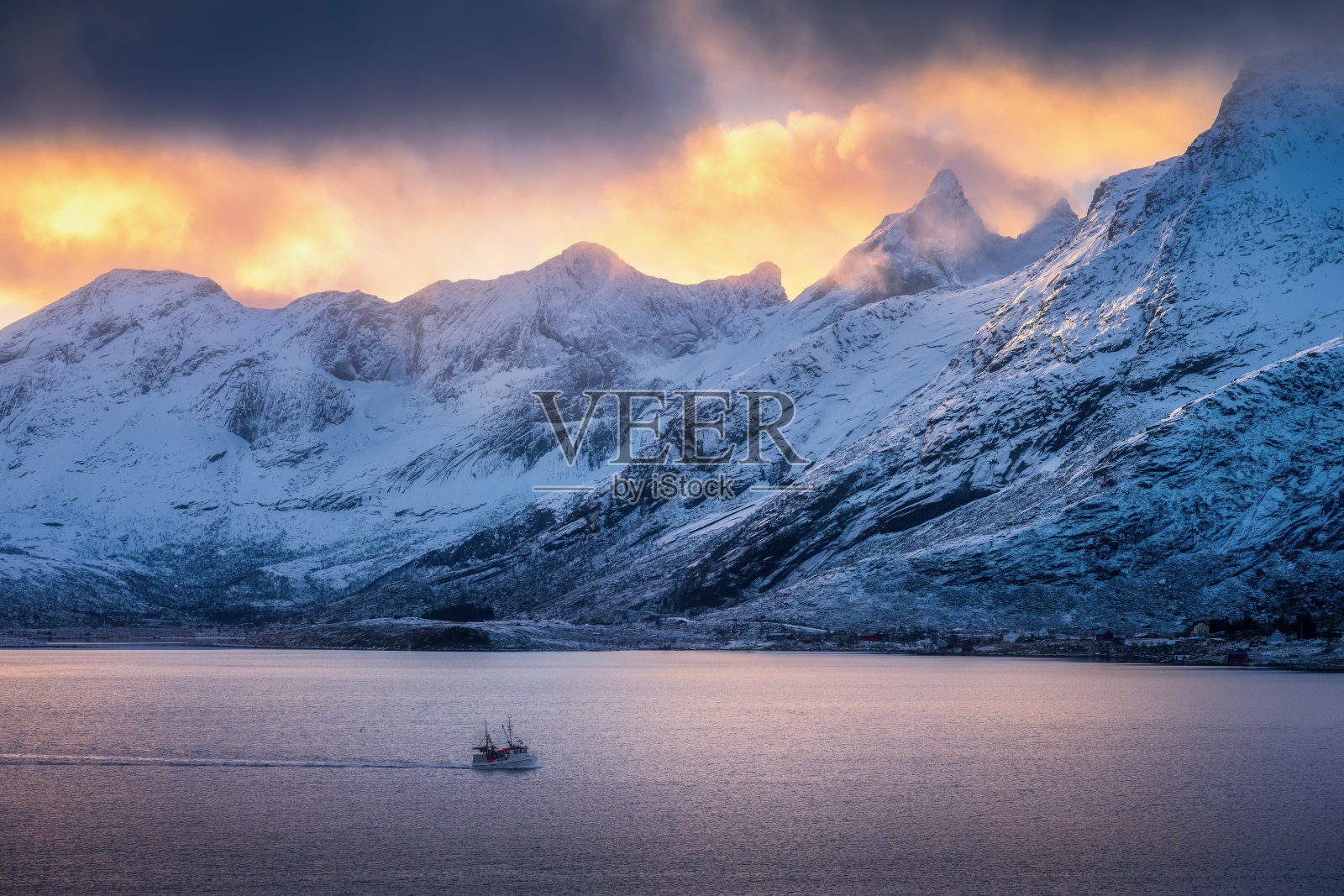 云雾中的雪山，明亮的阳光，冬季彩色日落时峡湾中的船只。挪威洛弗敦群岛。令人惊叹的风景，雪中的岩石、大海和金色阳光。北方海岸。自然。照片摄影图片