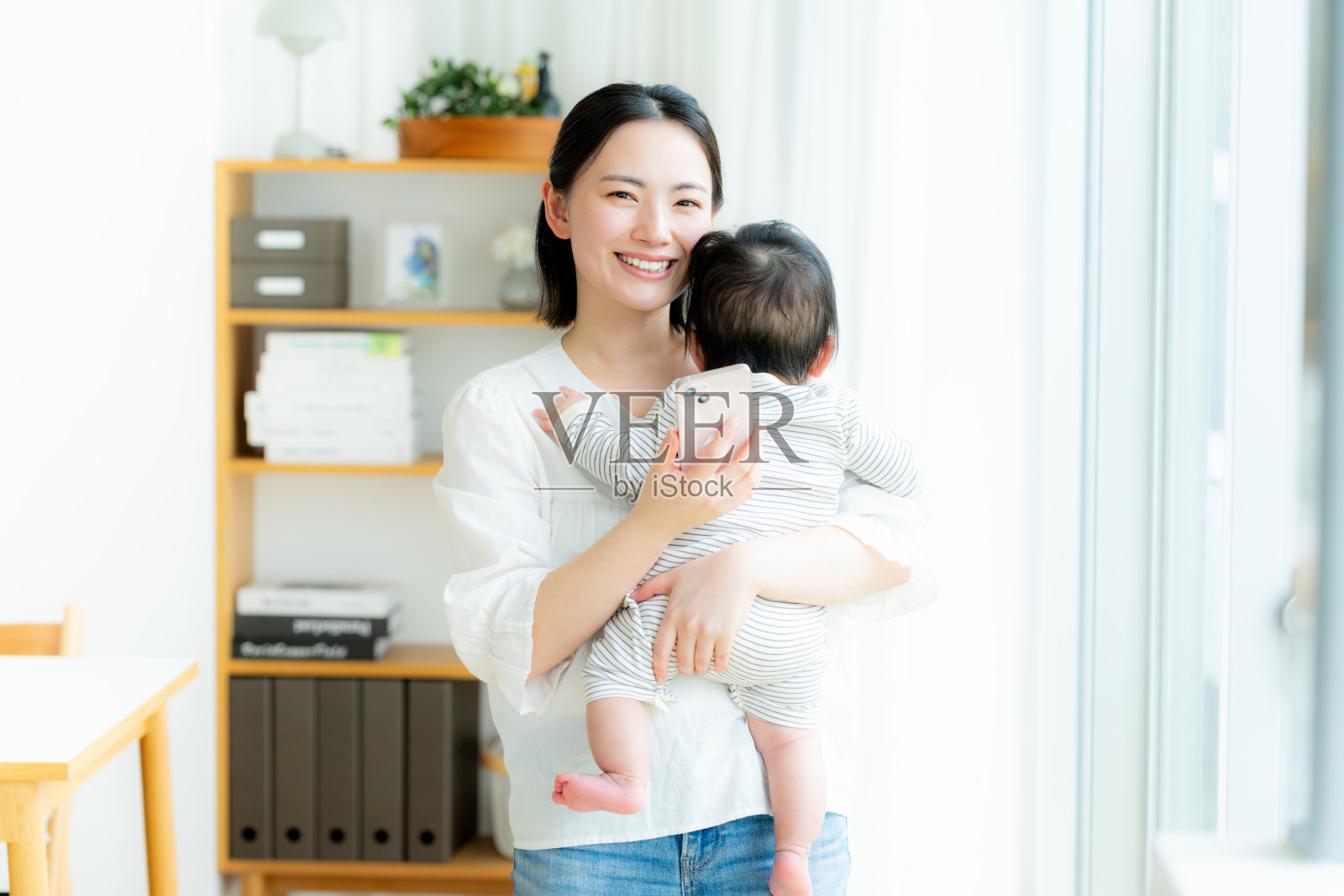 妈妈抱着婴儿，同时拿着智能手机照片摄影图片