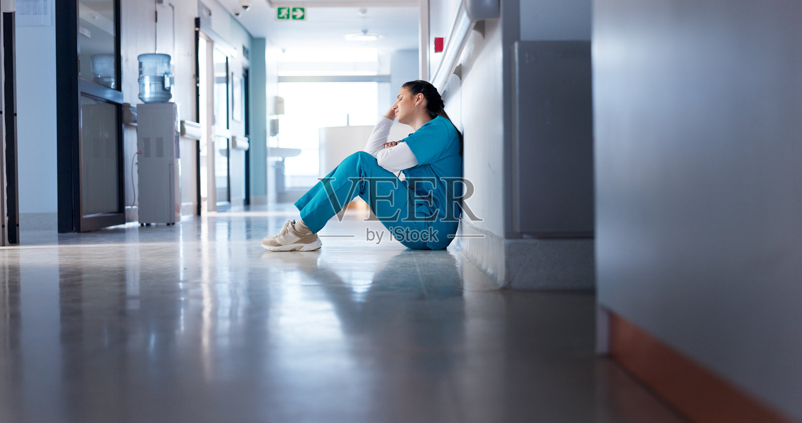 疲惫的女性医生在大厅中思考或感到沮丧，面临医疗挑战或错误。这个人在走廊中，承受着心理健康的压力，接收到坏消息和失败，感到疲惫不堪。照片摄影图片