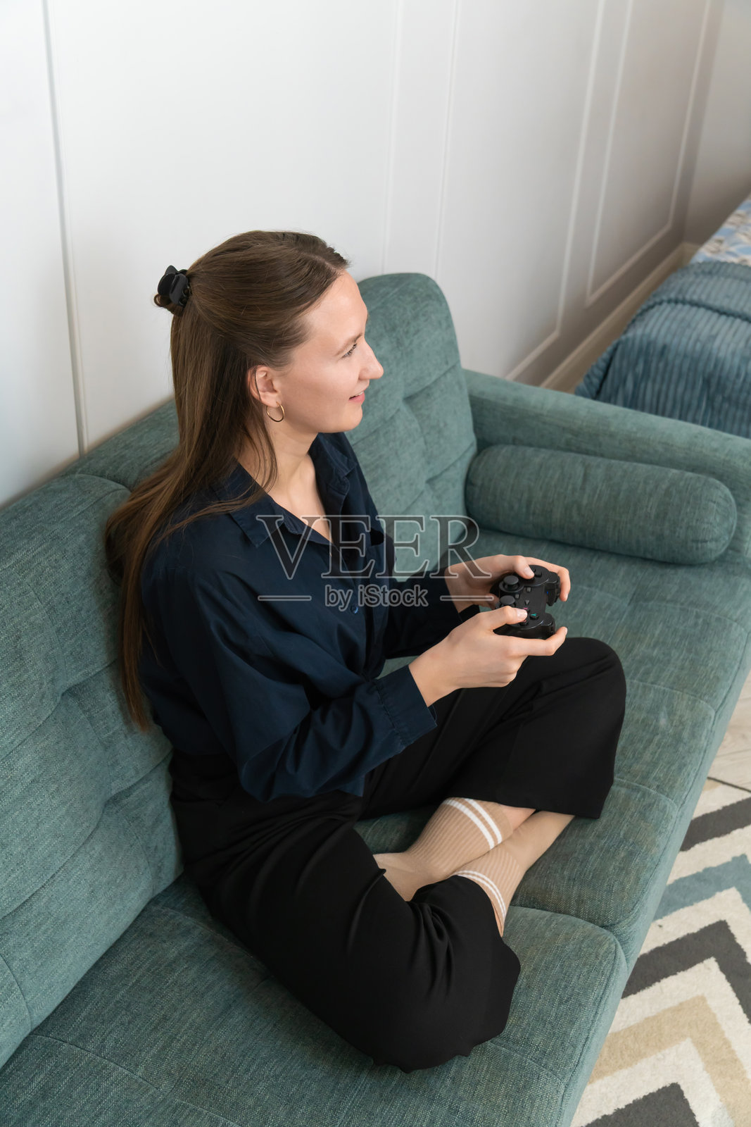 年轻女性舒适地坐在现代客厅的沙发上，手握游戏手柄，完全沉浸在玩视频游戏中，享受着愉悦和放松的闲暇时光。照片摄影图片