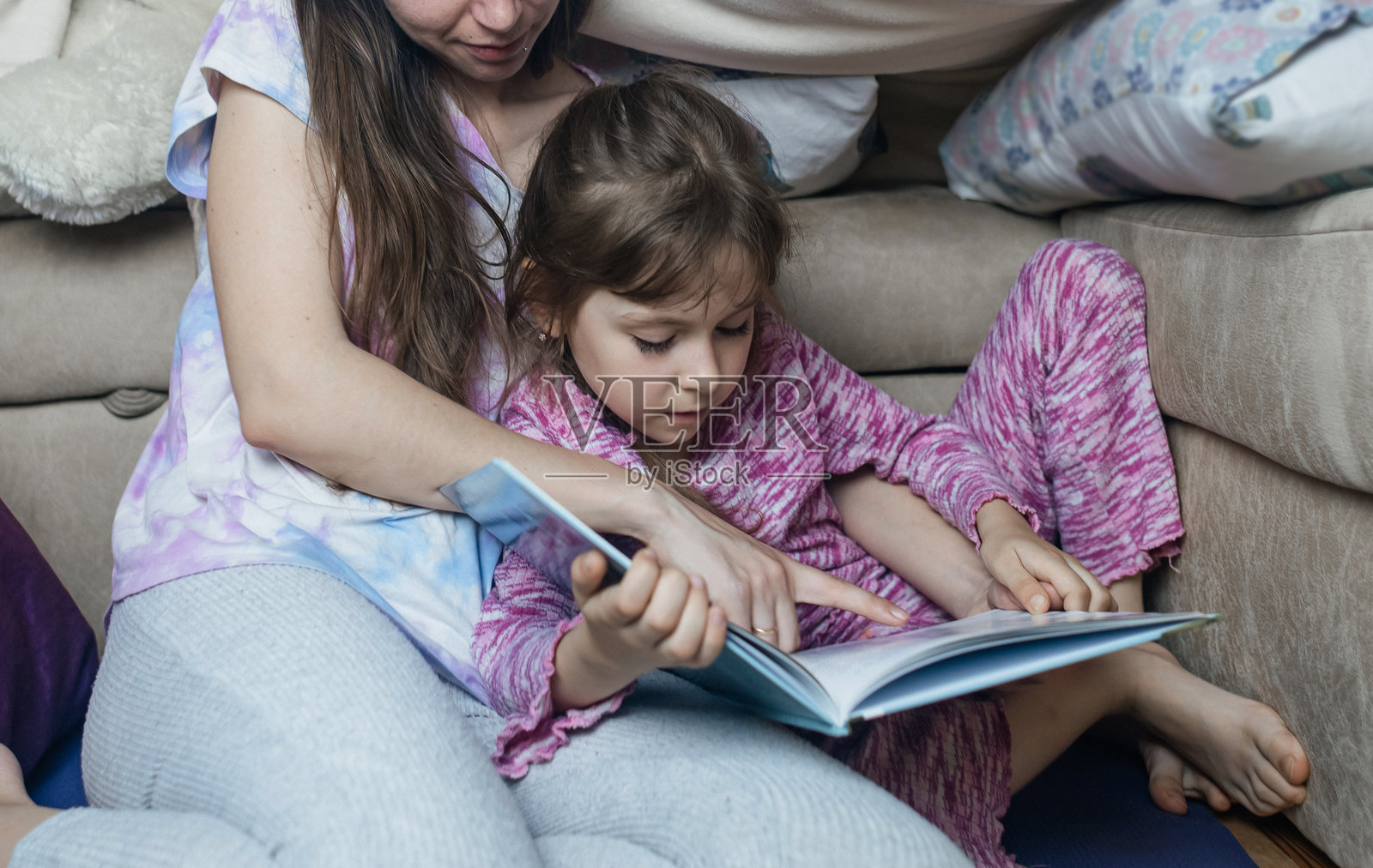 母亲和女儿坐在用毯子搭成的小屋里阅读一本书。与孩子们共度愉快的时光，睡前的宁静时光。照片摄影图片