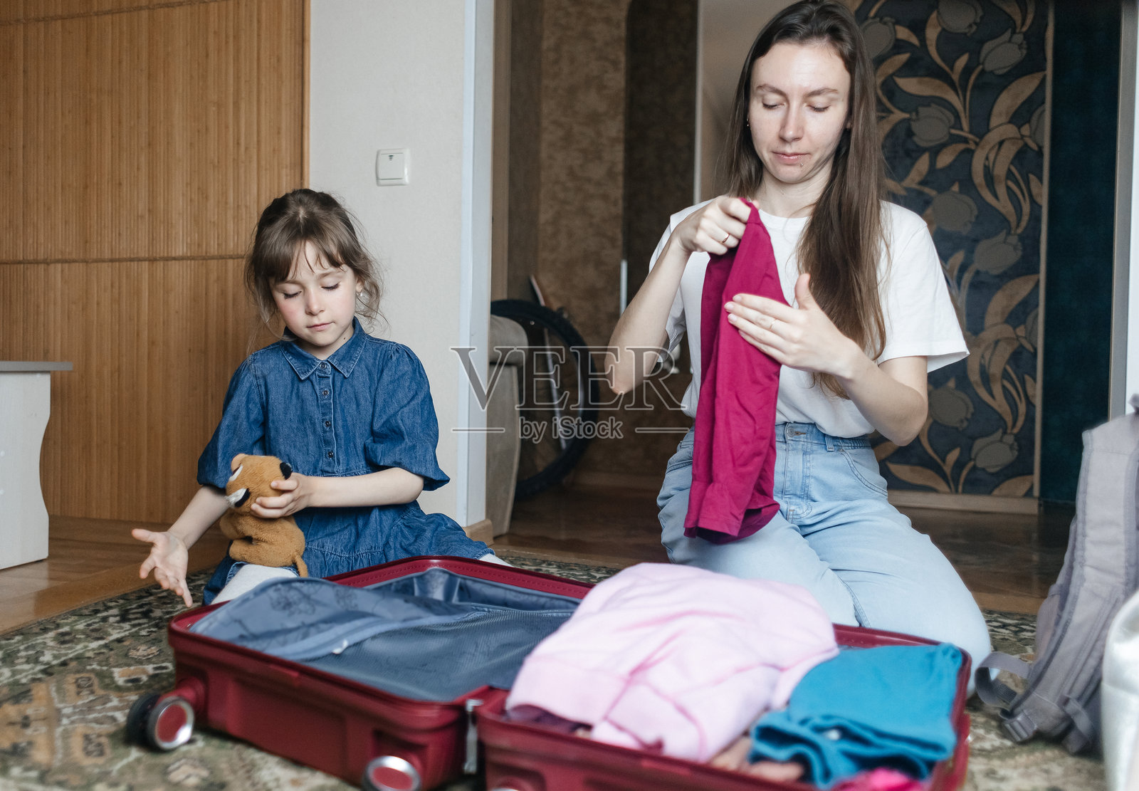 疲惫的母亲与6岁女儿一起打包旅行行李。旅行概念。旅行包的特写以及旅客疲惫的面孔。照片摄影图片