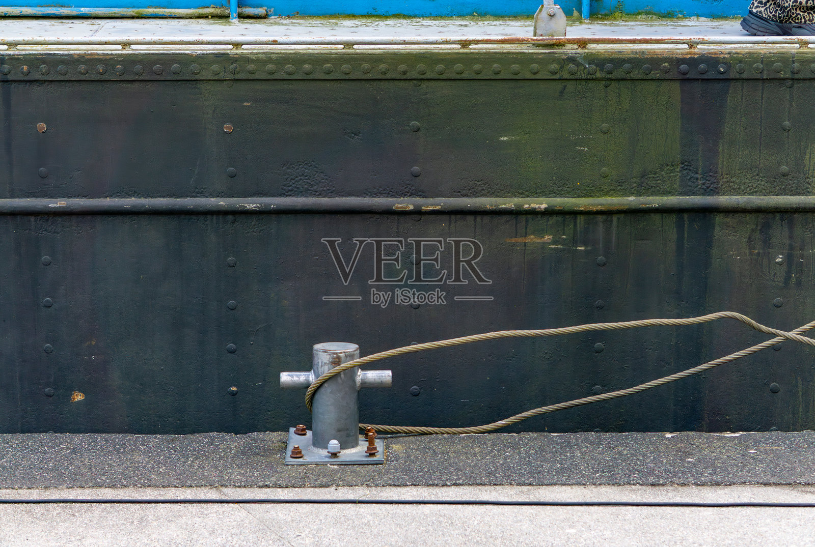 金属系船柱上缠绕着粗绳，位于大型船体旁边的码头上。海事停靠基础设施的功能细节。照片摄影图片