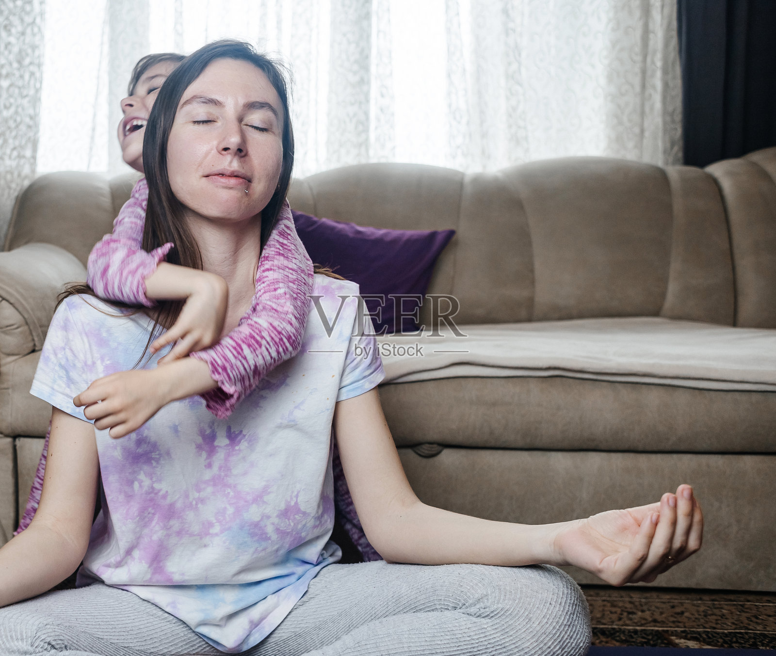 年轻妈妈试图冥想并在家锻炼，而她顽皮的女儿却不断打扰。家中的瑜伽被打断，展现了育儿的现实。妈妈和女儿一起玩得很开心。照片摄影图片