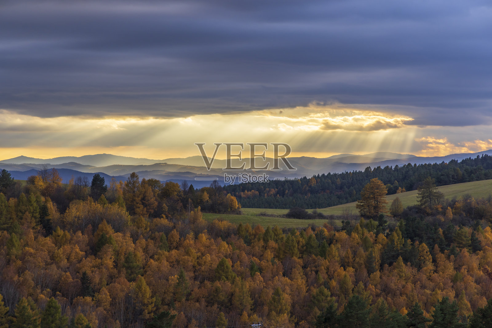 阳光透过云层洒在五彩斑斓的秋季森林景观上，背景是低塔特拉山脉。照片摄影图片