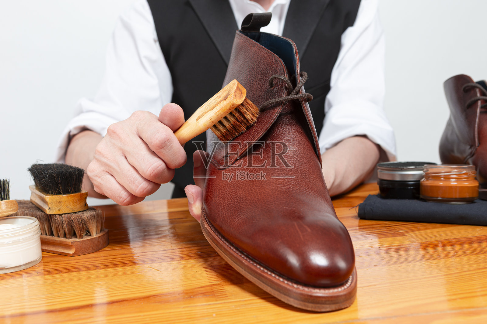 专业男鞋清洁工的手部特写，正在工作室中使用清洁刷清洁棕色德比皮靴。照片摄影图片
