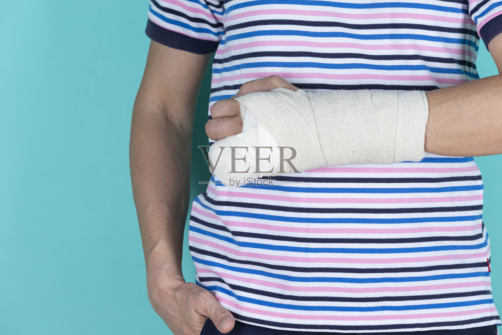 医疗概念。白人男性受伤的手被石膏和创可贴包扎，背景为青绿色。照片摄影图片