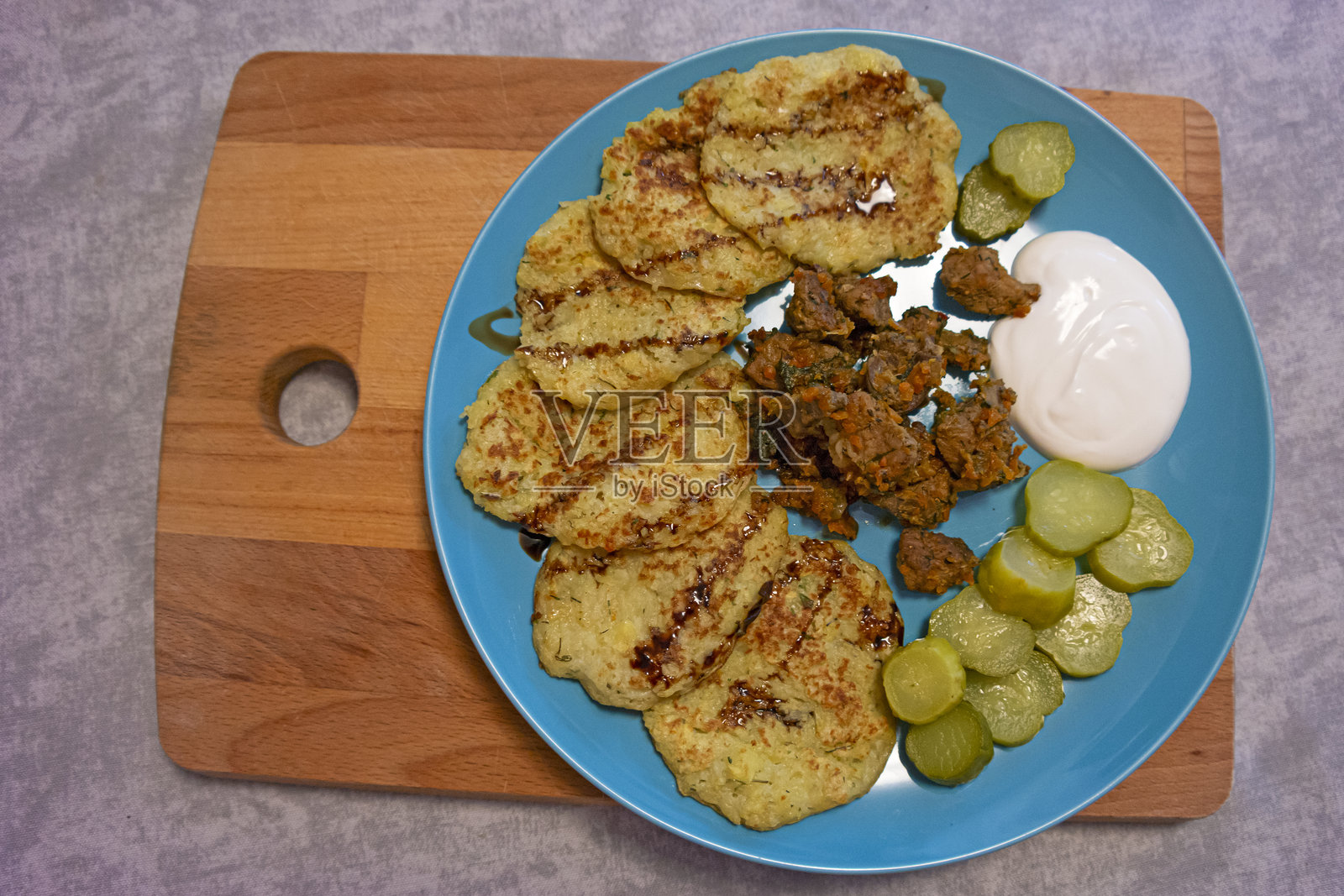 自制的西葫芦煎饼，上面放着酸奶油、烤猪肉和新鲜蔬菜，摆放在石灰灰色背景的盘子上方的俯视图照片摄影图片