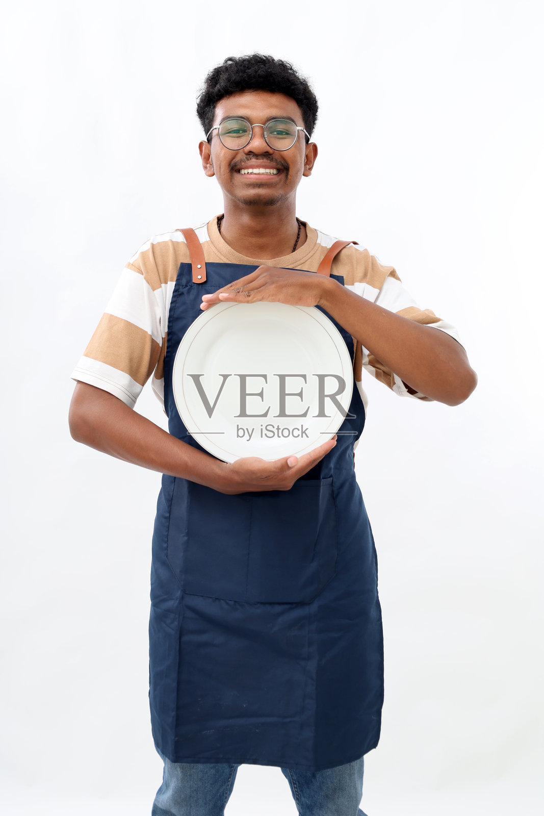 烹饪、烹饪艺术和人们的概念，快乐微笑的亚洲男子穿着围裙，手持干净的空盘子，背景为白色。照片摄影图片