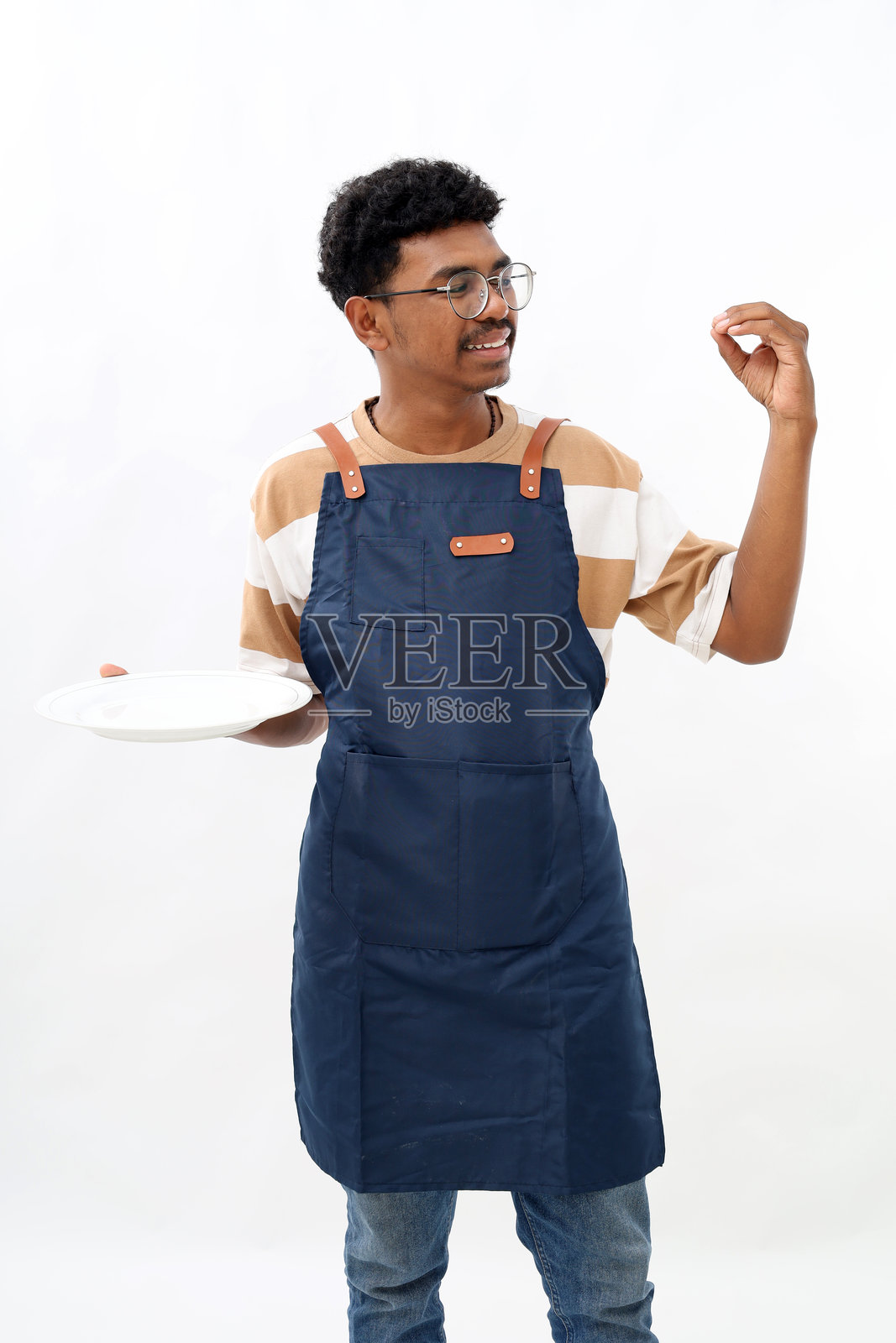 烹饪、烹饪艺术和人们的概念，快乐微笑的亚洲男子穿着围裙，手持空盘，展示美食标志，背景为白色。照片摄影图片