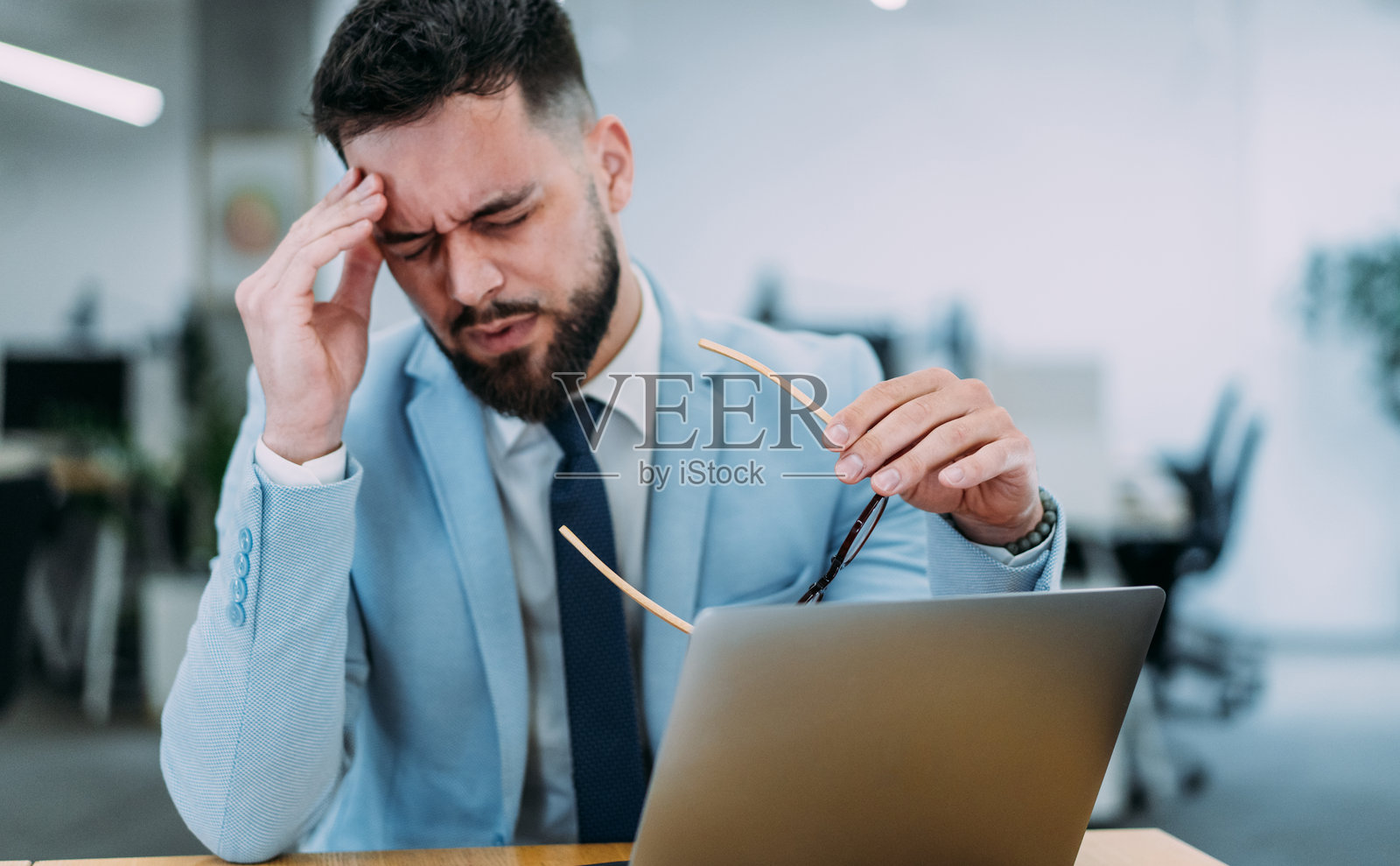 压力大的商人在办公室用笔记本电脑工作时感到头痛。照片摄影图片