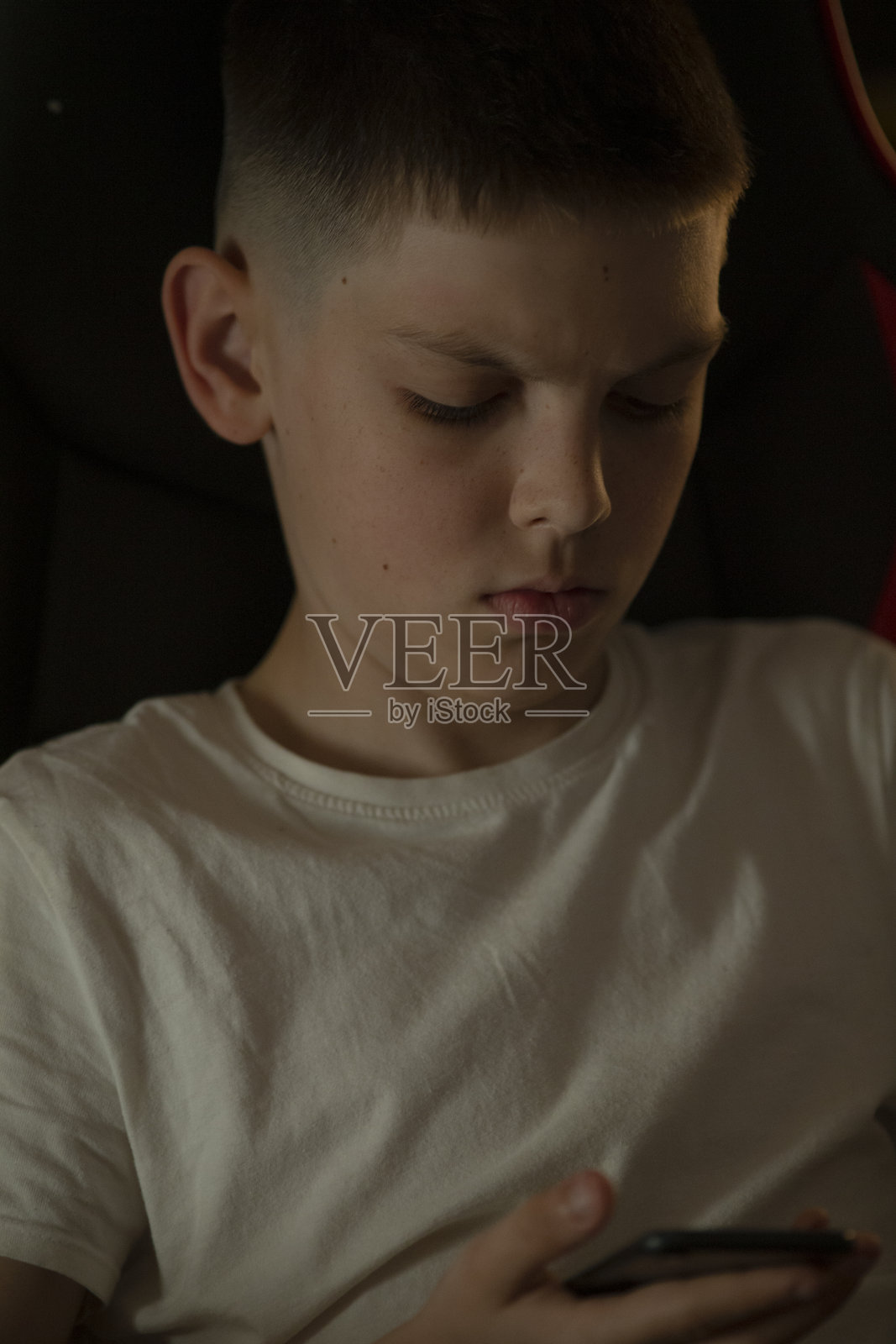 一个男孩在黑暗背景下专注地看着他的智能手机照片摄影图片