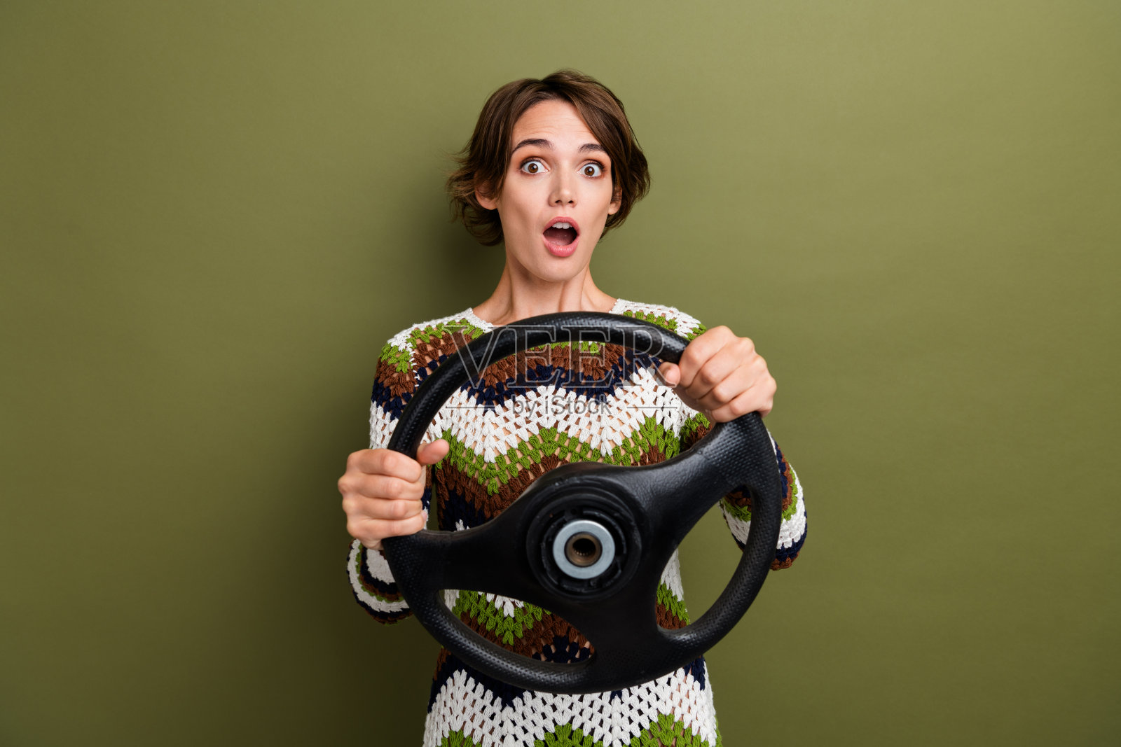 穿着条纹衣服的可爱惊讶女孩骑着汽车，背景为绿色。照片摄影图片