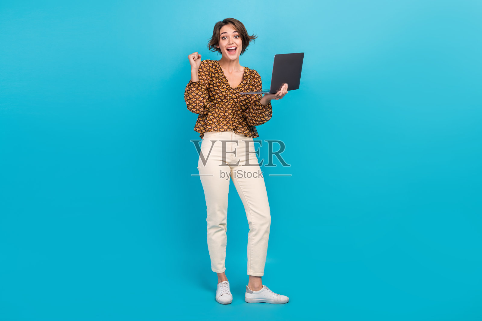 全身照，漂亮而开心的人使用笔记本电脑，举起拳头庆祝成功成就，背景为蓝色。照片摄影图片