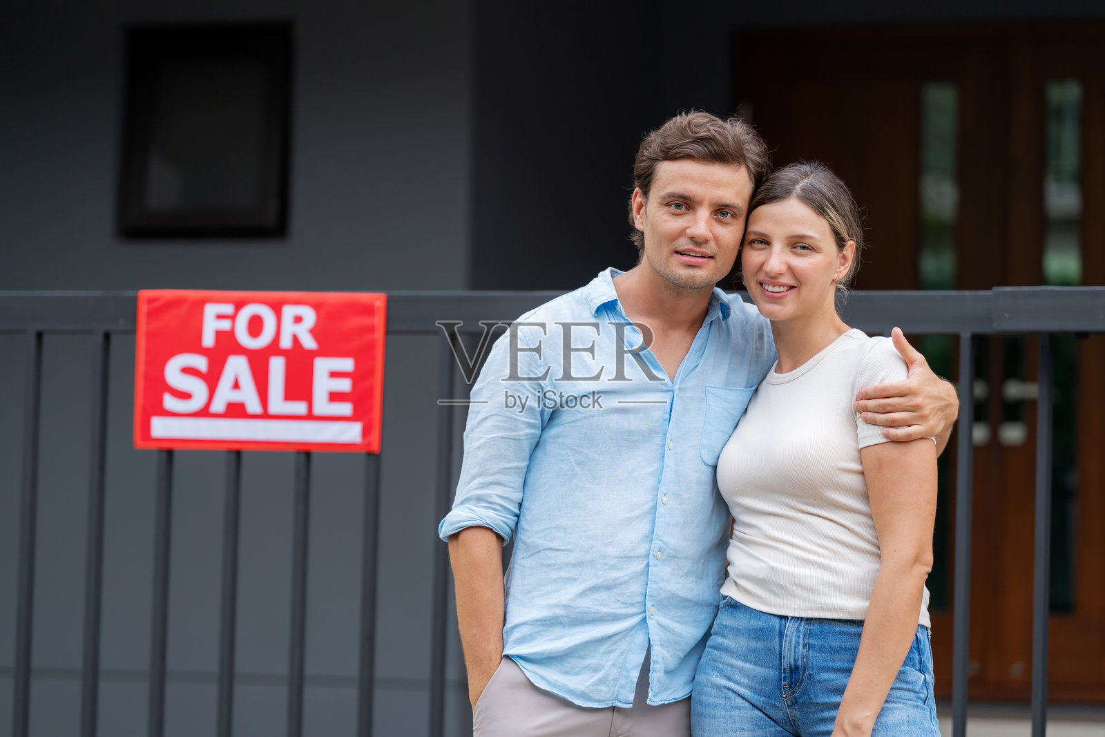 快乐的情侣站在他们以前的家前，手持“待售”标志，庆祝成功出售。这是一个成就的时刻，房地产成功和新的开始。他们微笑着自豪地一起向前迈进。照片摄影图片