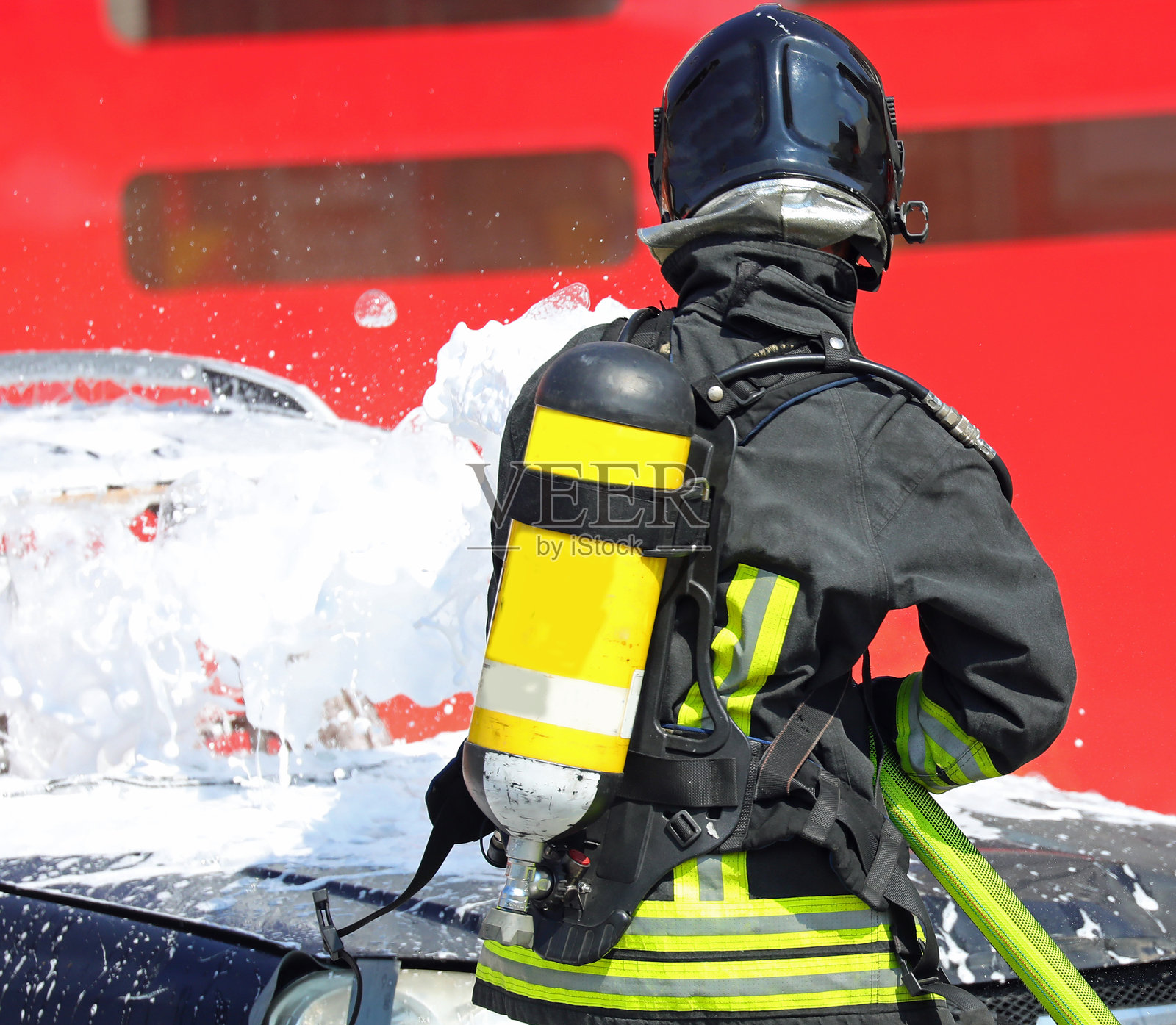 消防员肩上背着氧气瓶，向汽车喷洒泡沫灭火剂，以扑灭交通事故后的火灾。照片摄影图片