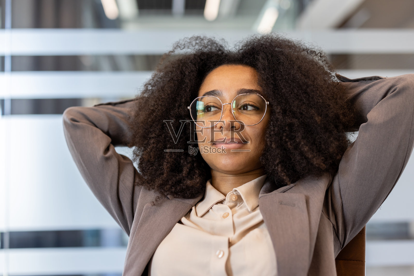 放松的年轻非裔美国女商人在办公室的椅子上坐着，双手放在头后，侧目而视，休息，满意于工作成果的特写照片照片摄影图片