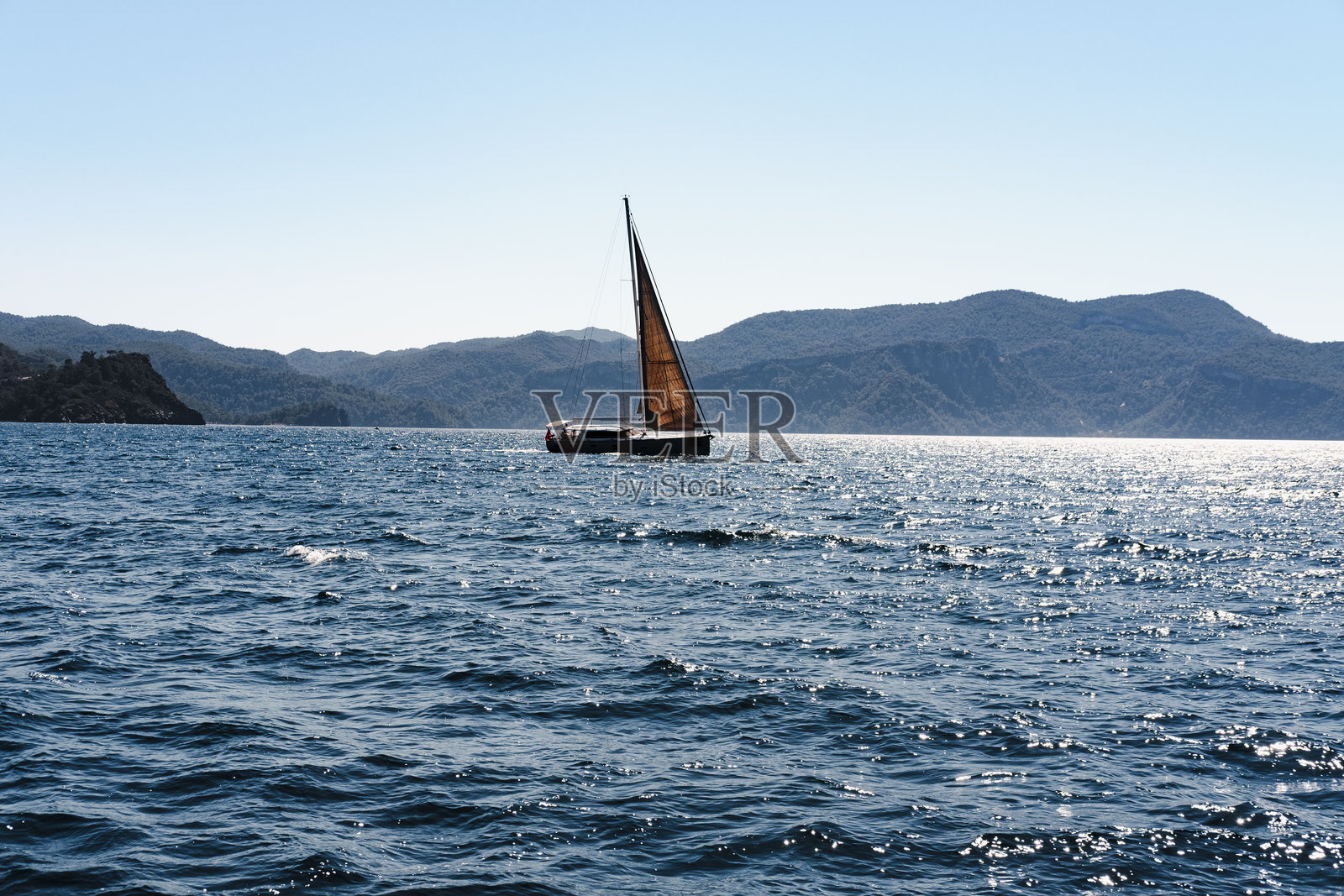 阳光明媚的日子，海面上航行的帆船，背景是山海相连，完美的奢华航海冒险。照片摄影图片