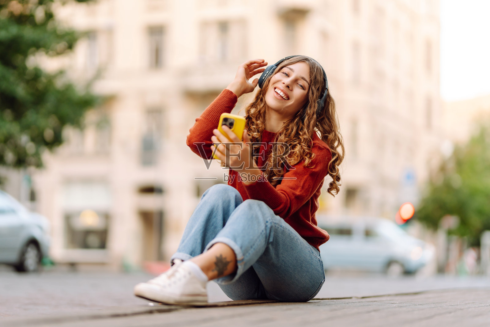 时尚女性在阳光明媚的街道上戴着无线耳机，使用手机听音乐。照片摄影图片