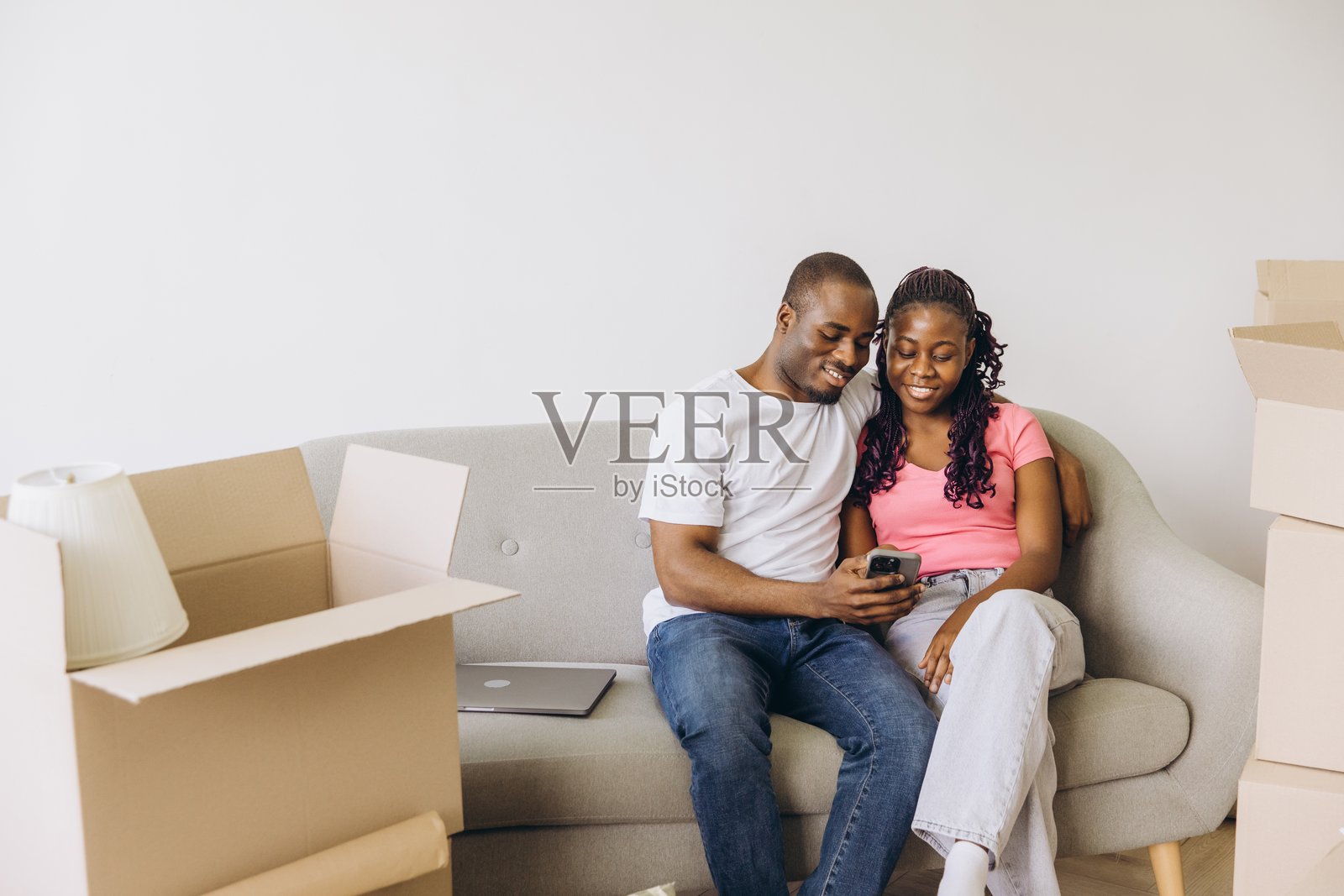 非裔美国夫妇在沙发上放松，使用智能手机，同时搬入新家照片摄影图片
