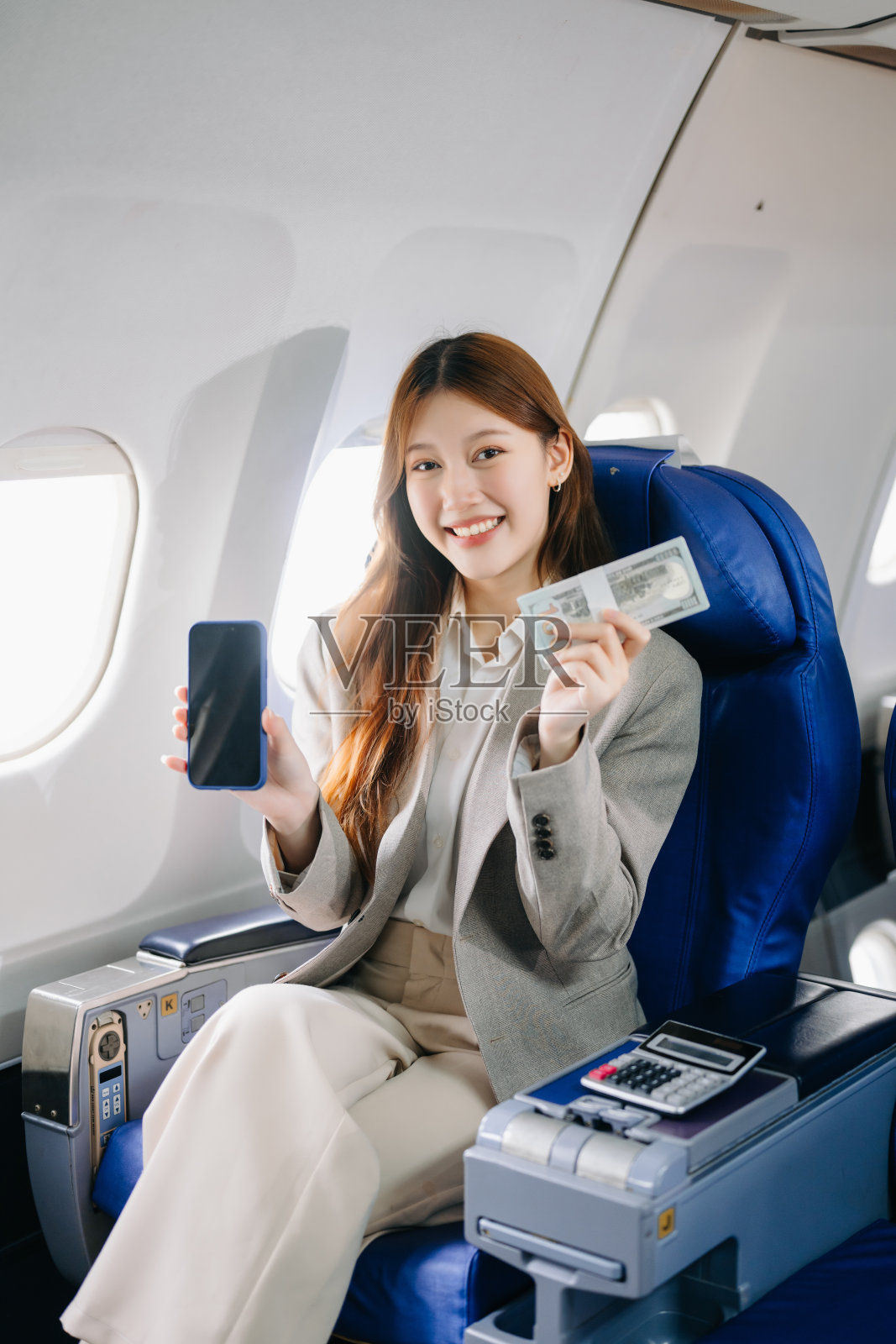 年轻的亚洲高管在头等舱中表现出色，同时使用数字平板、笔记本电脑和智能手机进行多任务处理，适用于金融、旅行和生活方式。照片摄影图片