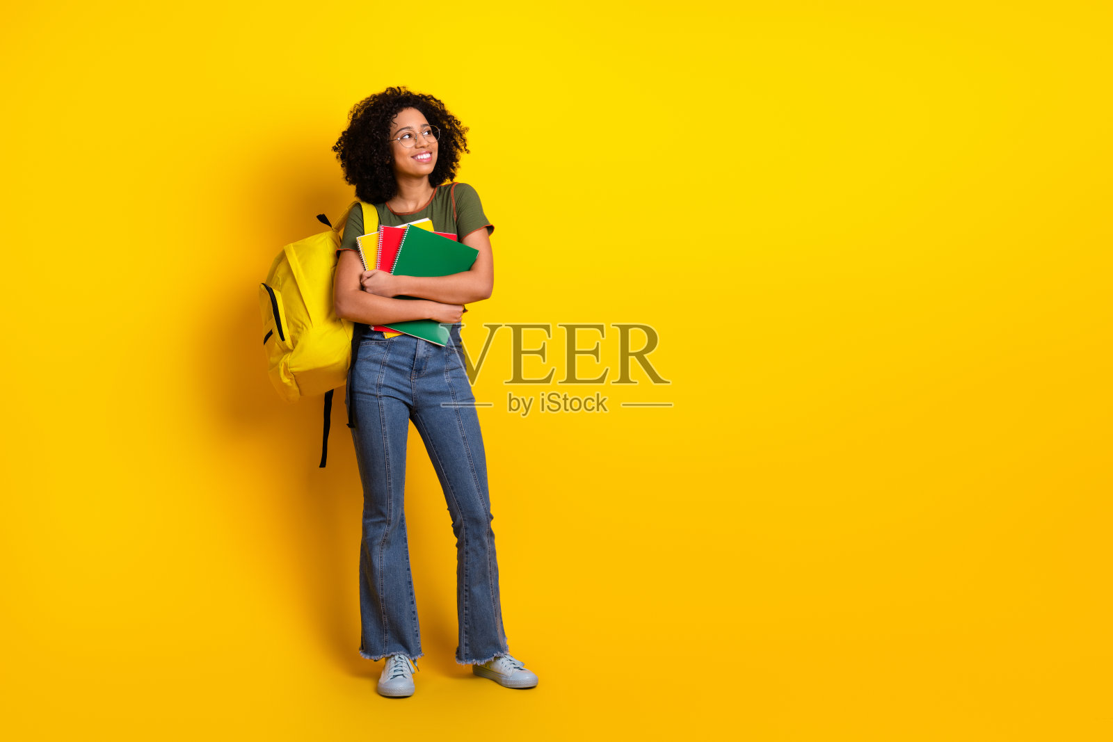 自信的年轻学生背着书包和书本，站在鲜艳的黄色背景前照片摄影图片