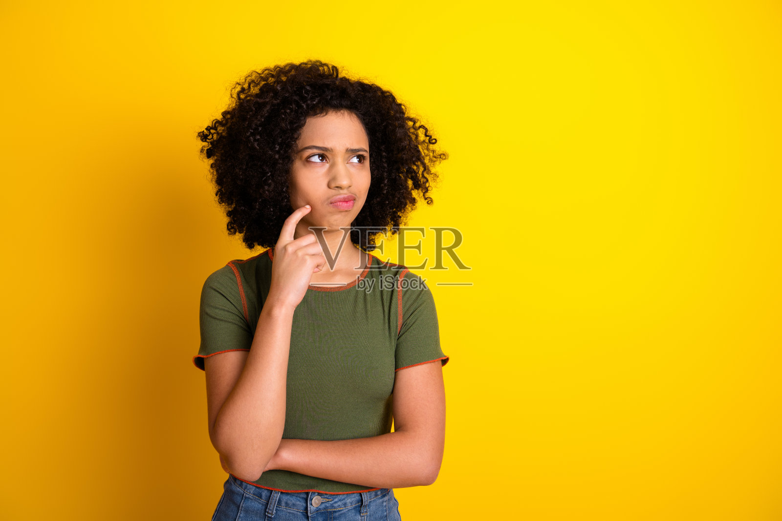 迷人的年轻女性，面带沉思表情，穿着休闲服装，摆姿势于鲜艳的黄色背景前。照片摄影图片