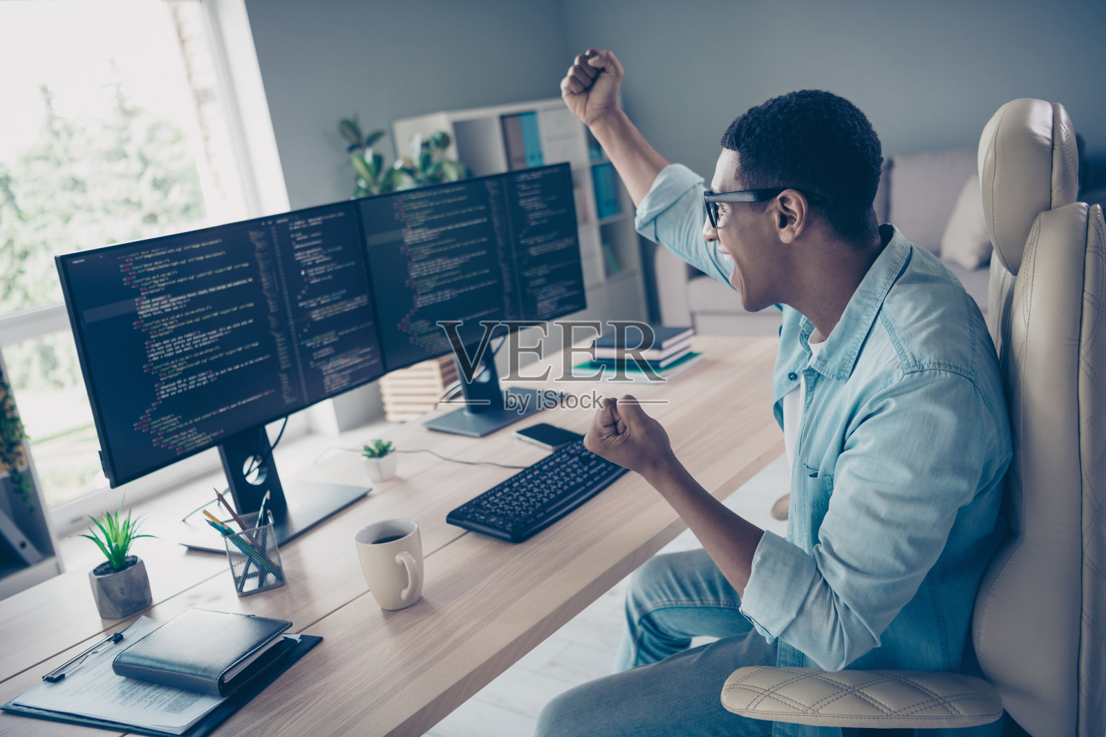 侧面拍摄一位疯狂的年轻人庆祝他的代码没有错误，他举起拳头欢呼，软件开发者在办公室工作区。照片摄影图片