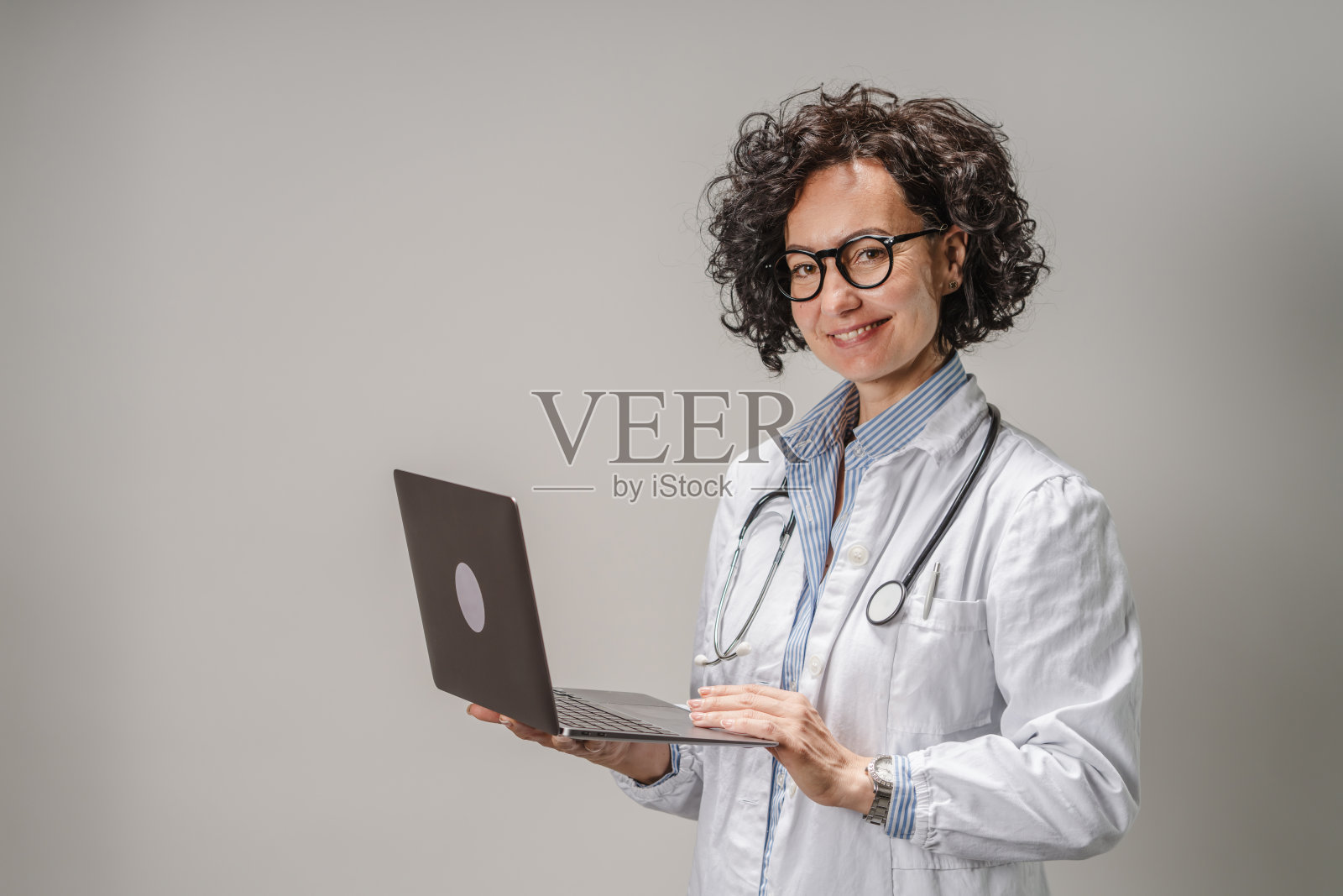 美丽的女医生在白色背景的摄影棚中手持笔记本电脑照片摄影图片