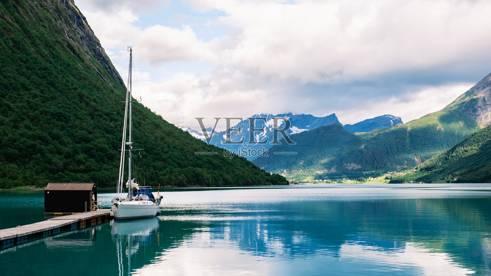 挪威阳光明媚的日子里，宁静的峡湾风景中有一艘帆船和雄伟的山脉。照片摄影图片
