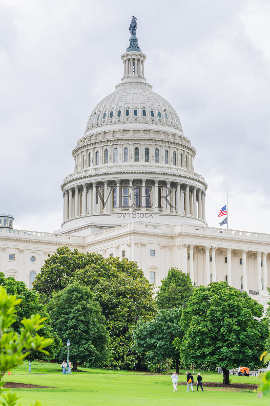游客在华盛顿特区的国会大厦穹顶下的郁郁葱葱的场地上漫步，天气阴云密布。照片摄影图片