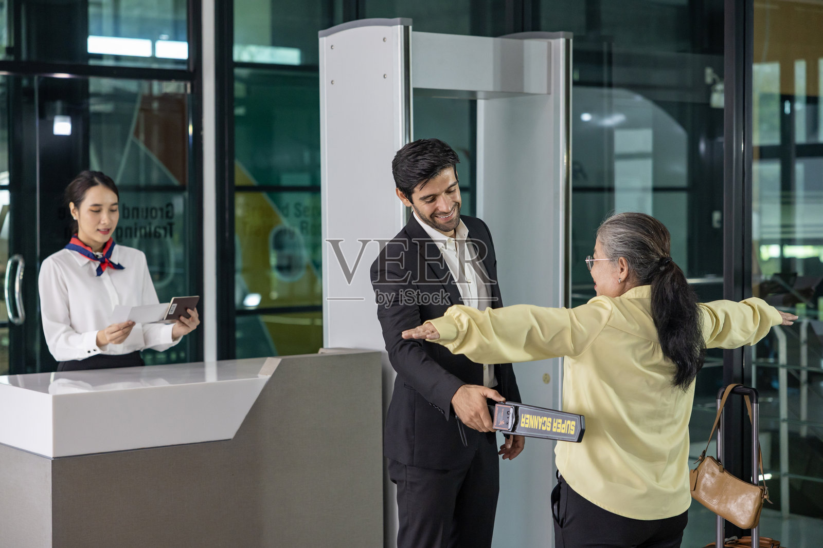 航空公司地面工作人员在机场出发大厅使用金属探测器对每位乘客进行安全检查，以确保登机前的安全协议。照片摄影图片