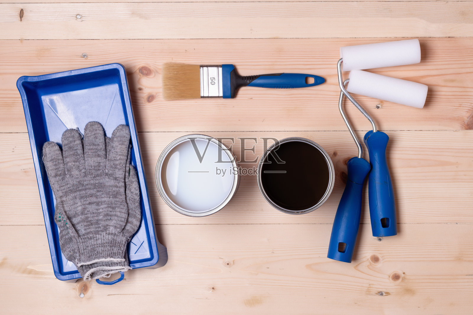 地板饰面选择，展示了两个打开的涂料罐，旁边有滚筒、刷子、手套和托盘，放在木质表面上，装修困境。照片摄影图片
