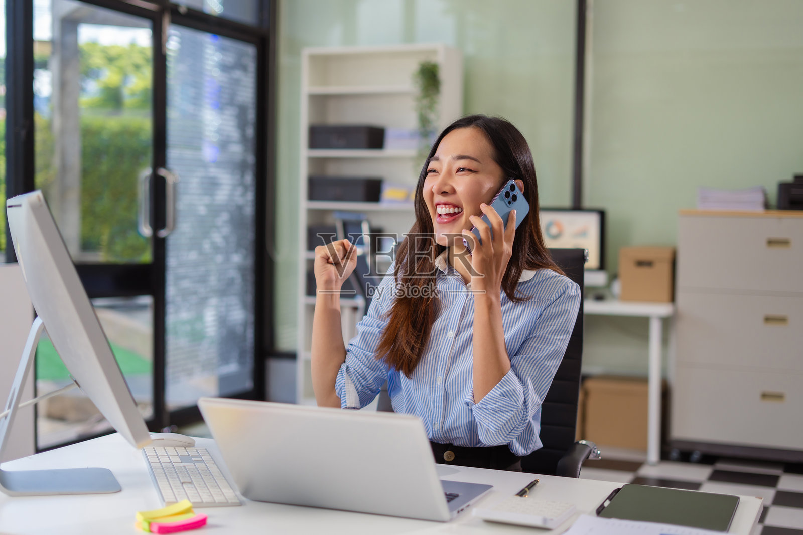 兴奋迷人的女性商务工作者在办公室使用智能手机和笔记本电脑工作，感到快乐。照片摄影图片