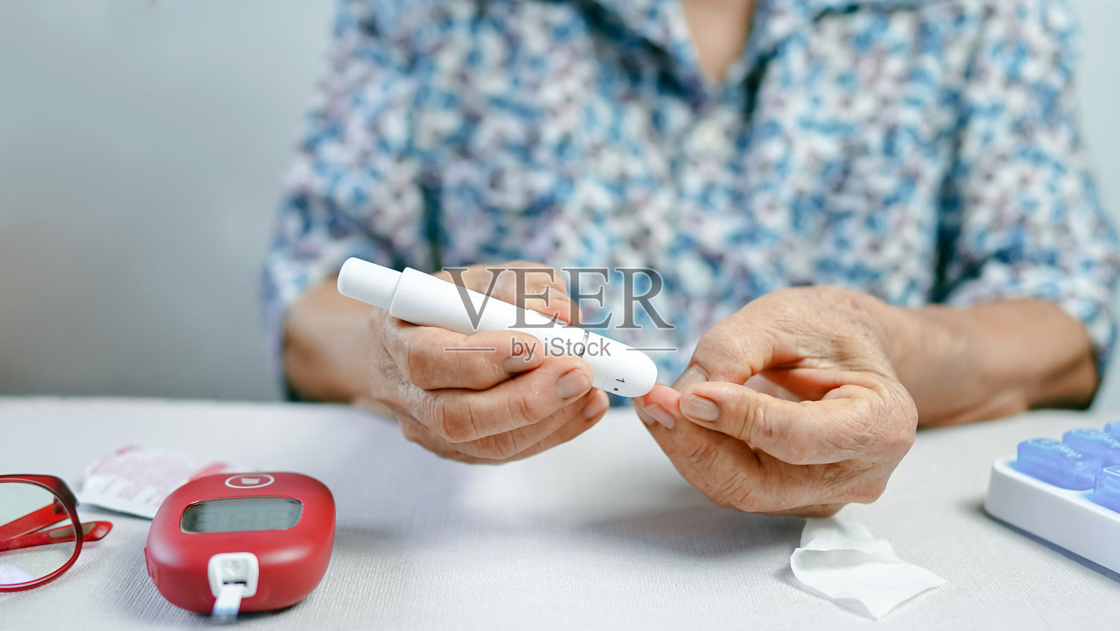 老年人用穿刺装置刺破手指，在白色桌子上使用糖尿病监测工具测试血糖。照片摄影图片