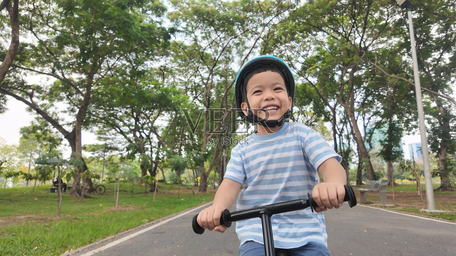 快乐的小亚洲男孩在公园绿树成荫的小路上骑着平衡车。照片摄影图片