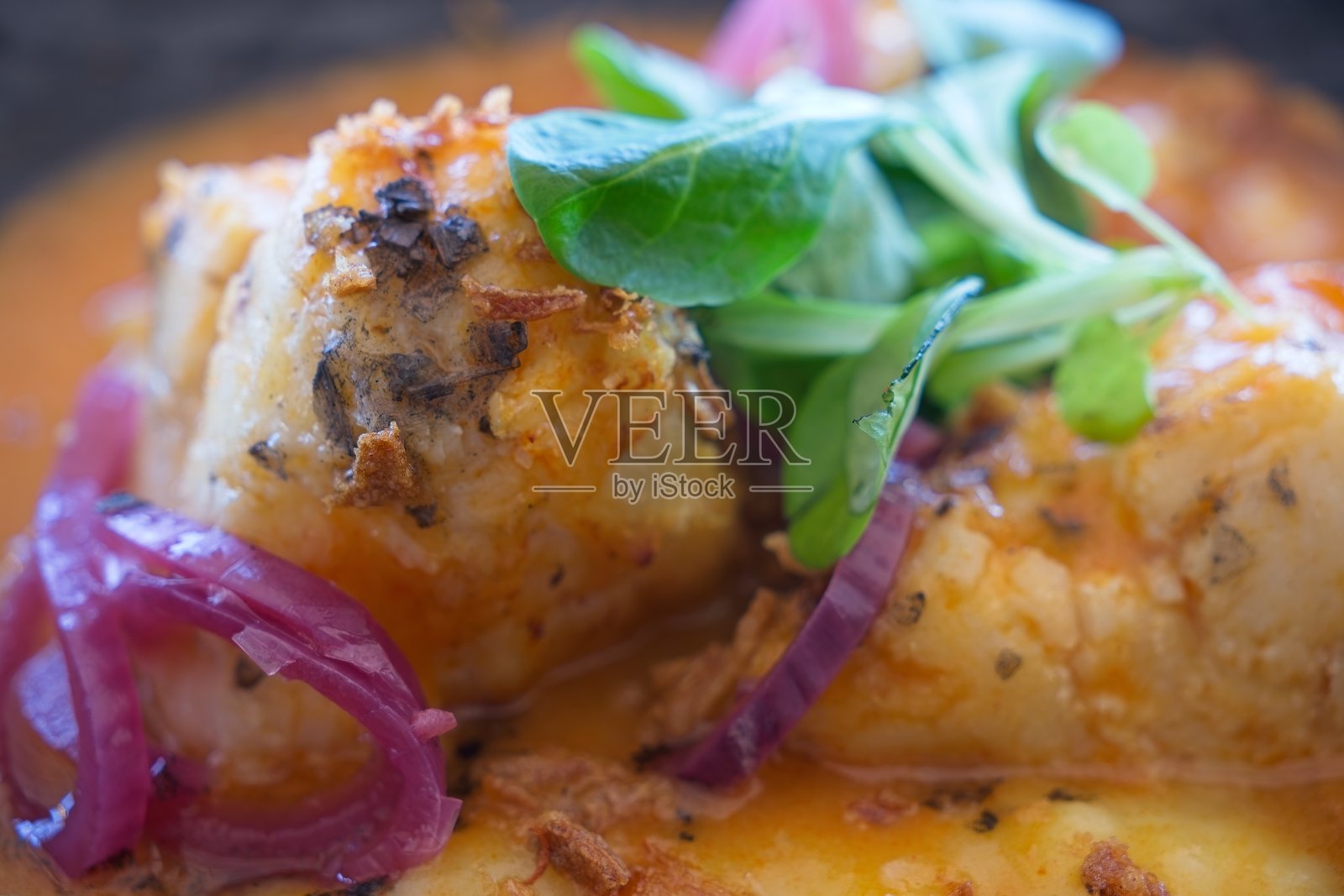 monkfish fillet resting on rustic plate, garnished with sliced red onions, aromatic herbs, drizzled with zesty orange sauce照片摄影图片