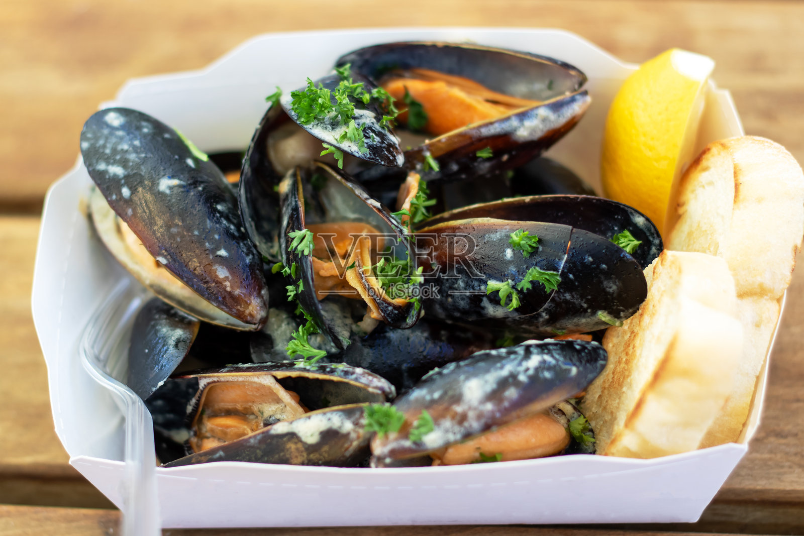 一个装满贻贝和面包的纸容器放在桌子上。照片摄影图片